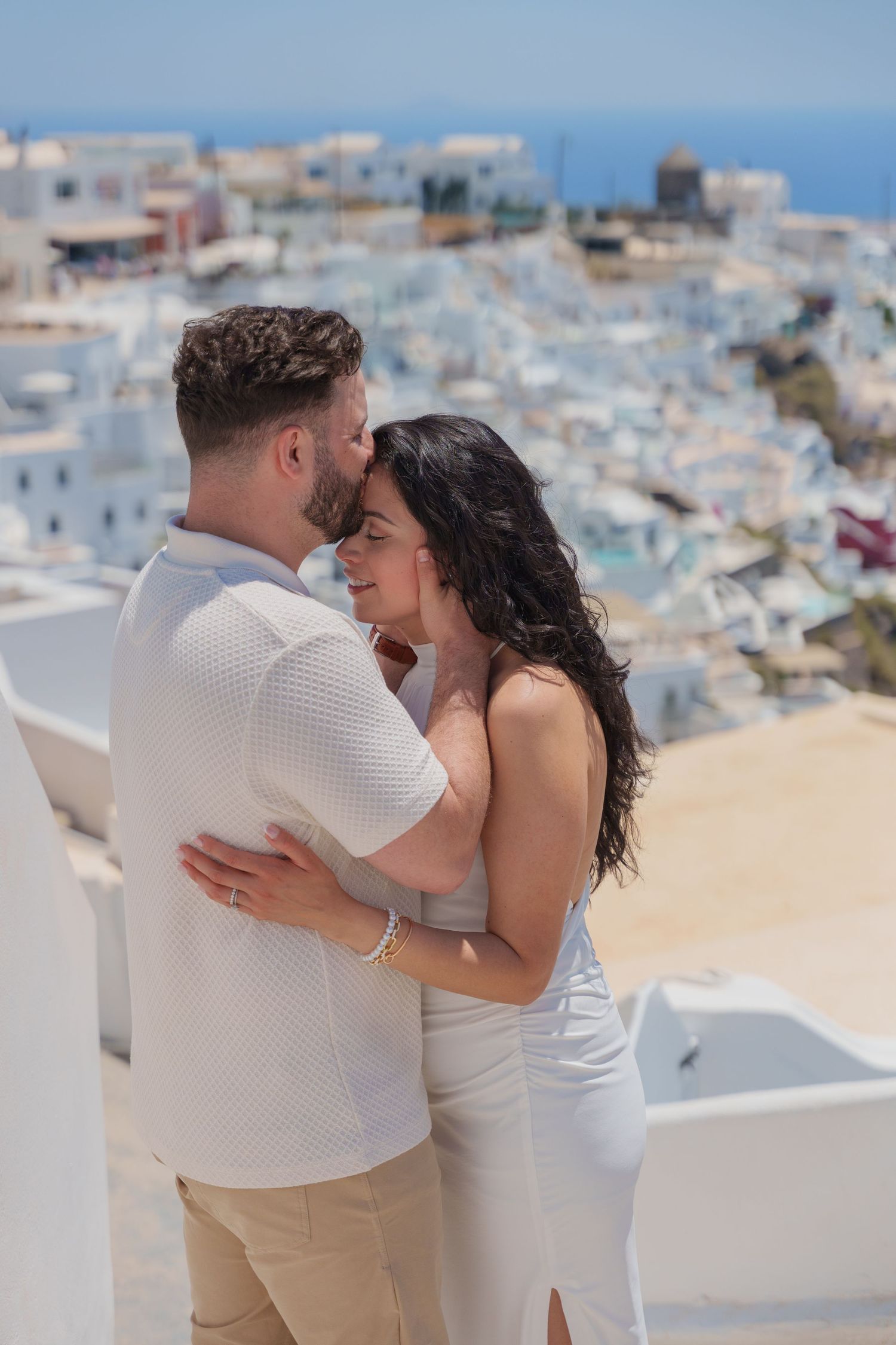 Couple kissing on a Santorini cliff in front of the white-washed houses during a lifestyle photoshoot, enjoying natural light