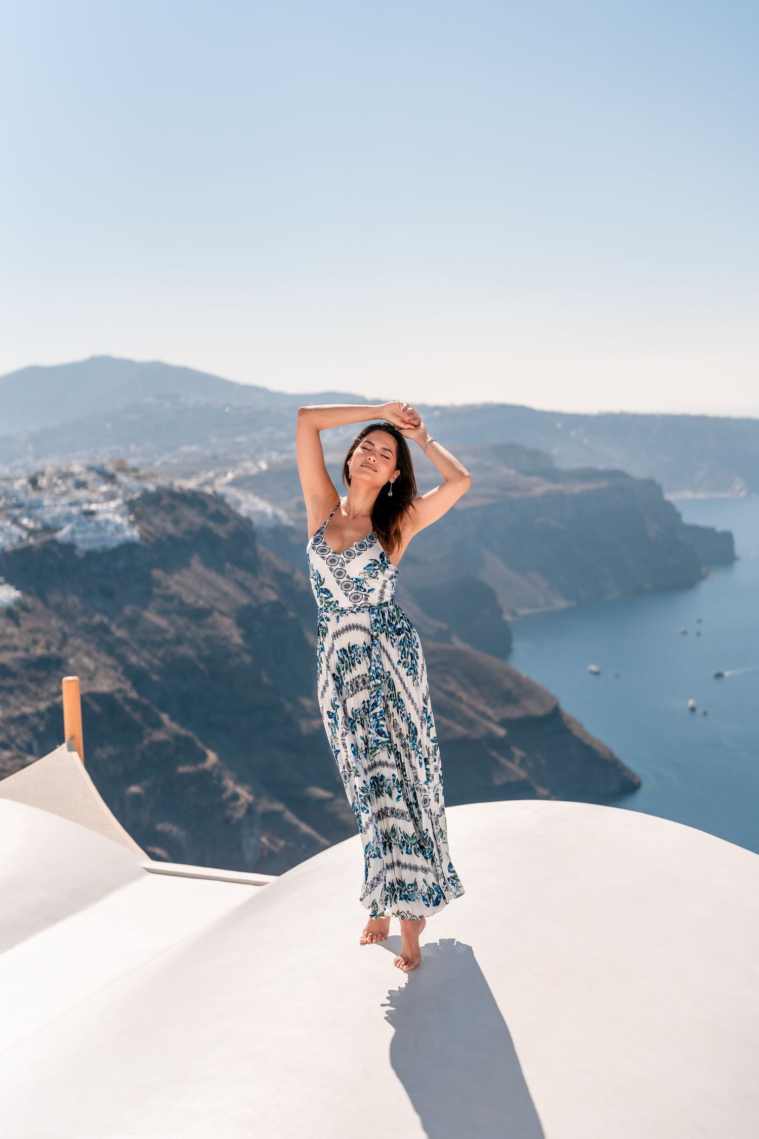Model, Andrea Meza Miss Universe 2020 on Santorini caldera on a white terrace dome during a lifestyle photoshoot, enjoying natural light.