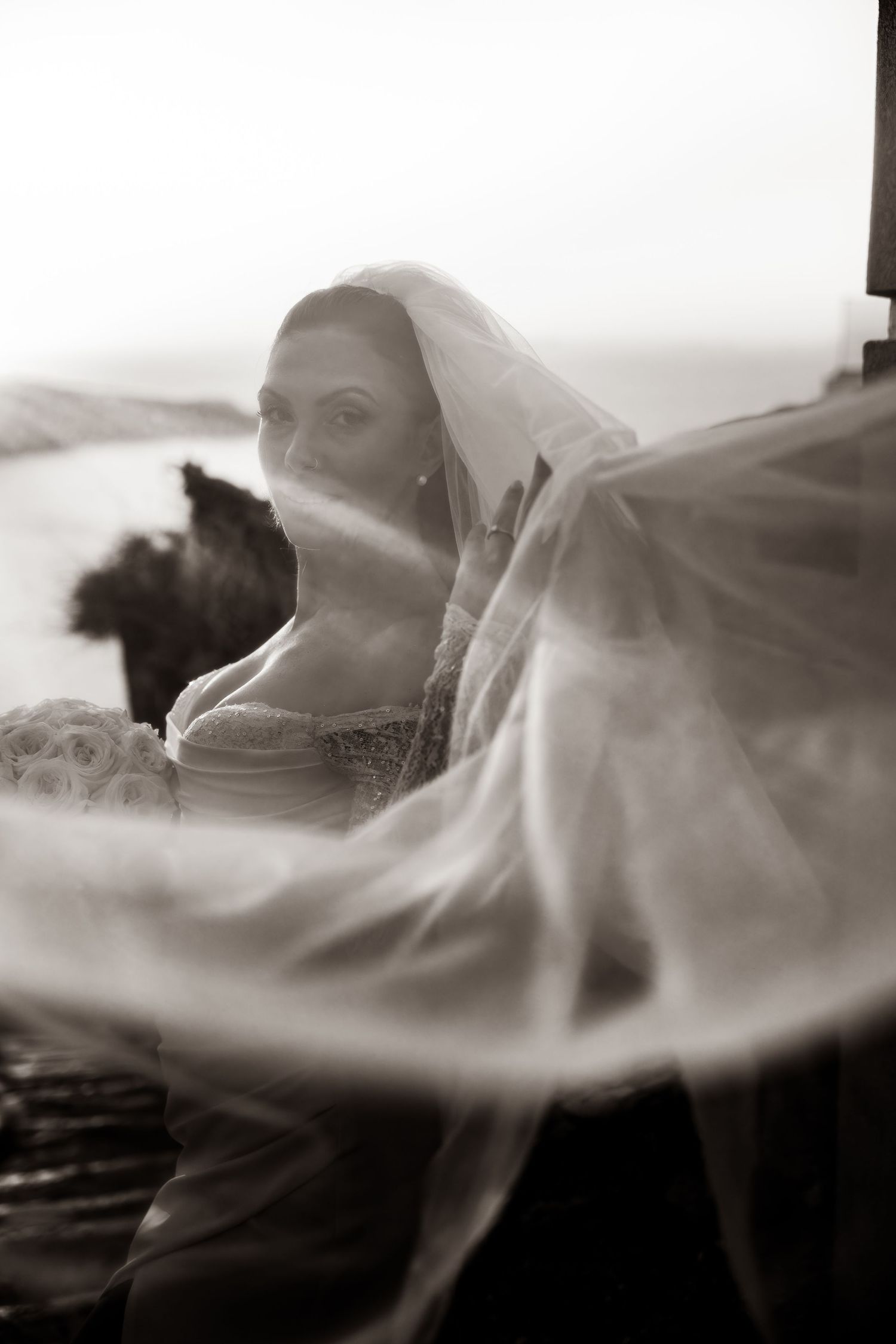 A romantic wedding moment of a bride embracing her veil in the air, captured on a Santorini cliff, celebrating love and togetherness