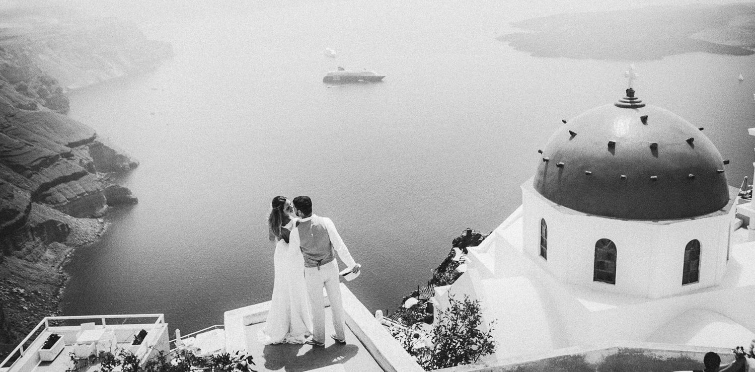 Elopement moment captured on a Santorini terrace next to blue domes, intimacy, love and laughter in the air at the caldera view
