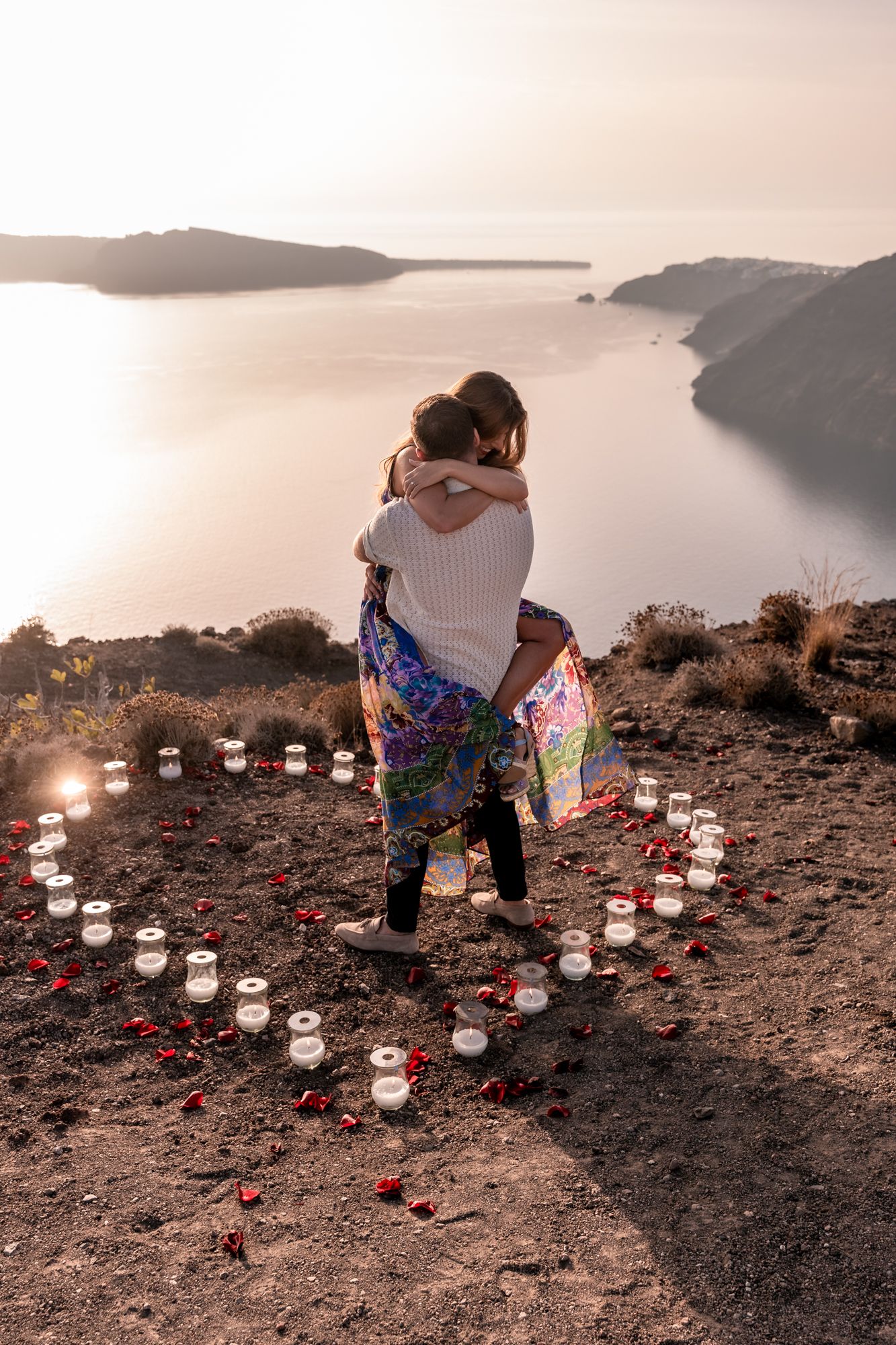 Groom proposing to bride in Santorini cliffs with flowers, capturing the magical yes moment filled with timeless emotions and love