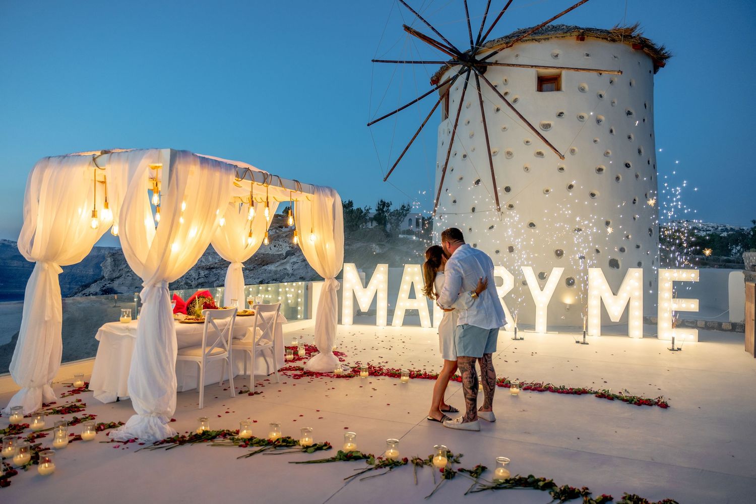 Groom proposing to bride in Santorini with flowers, capturing the magical yes moment with windmill background