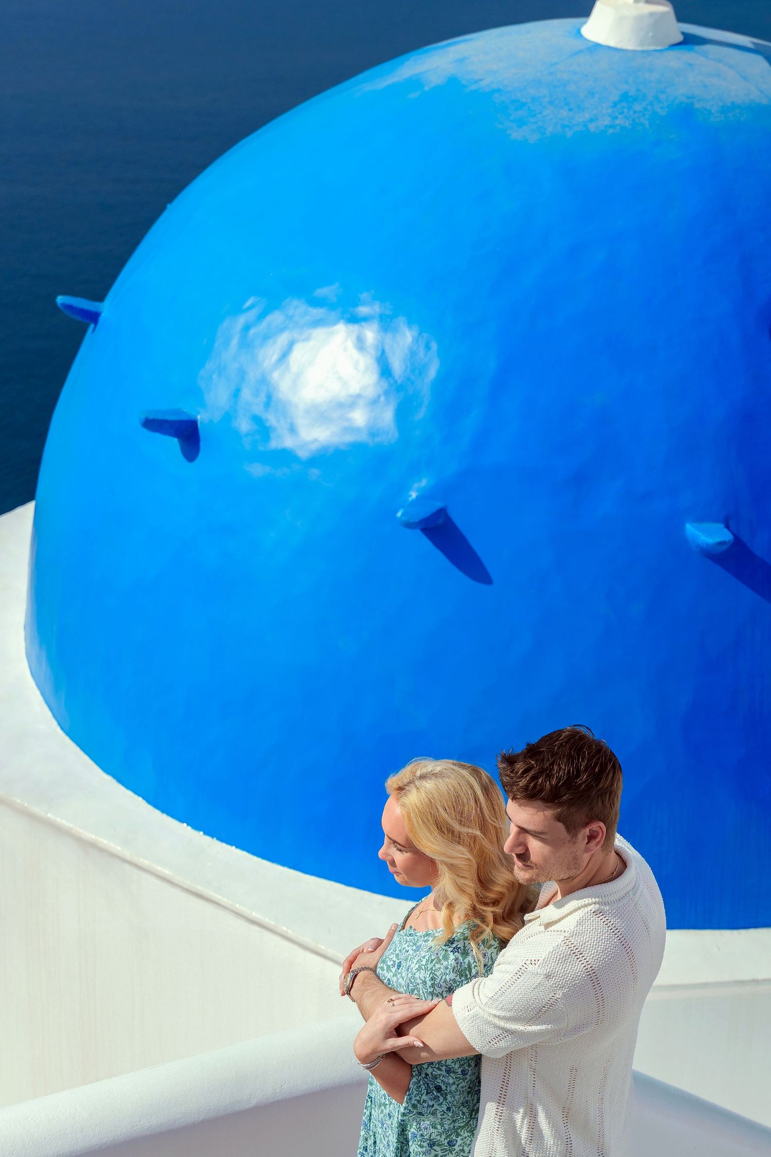 Romantic lifestyle photoshoot of a couple on a Santorini terrace, in front of blue dome, natural light and love moments