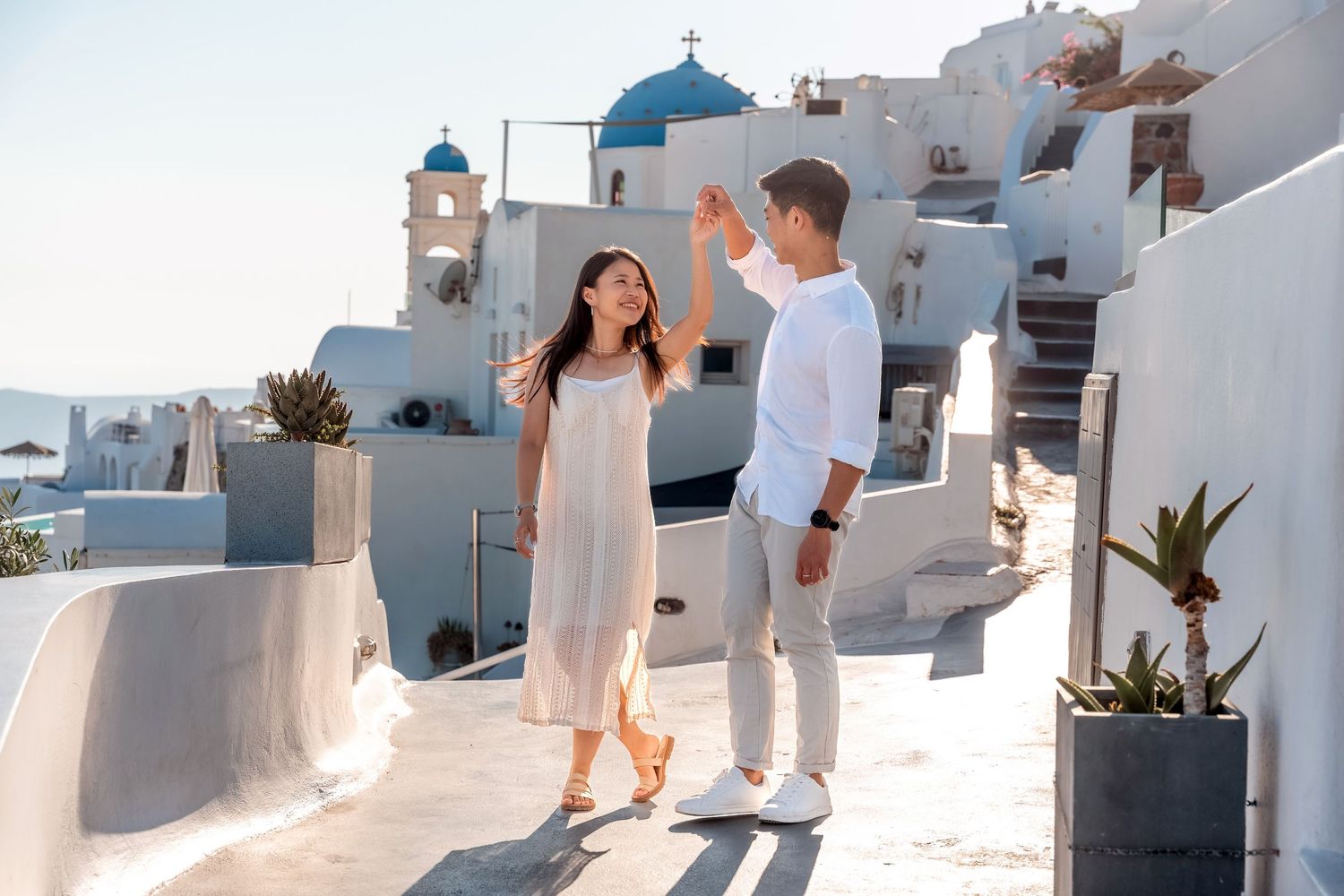 Partners walking hand in hand in a white-washed village in Santorini, intimate and joyful