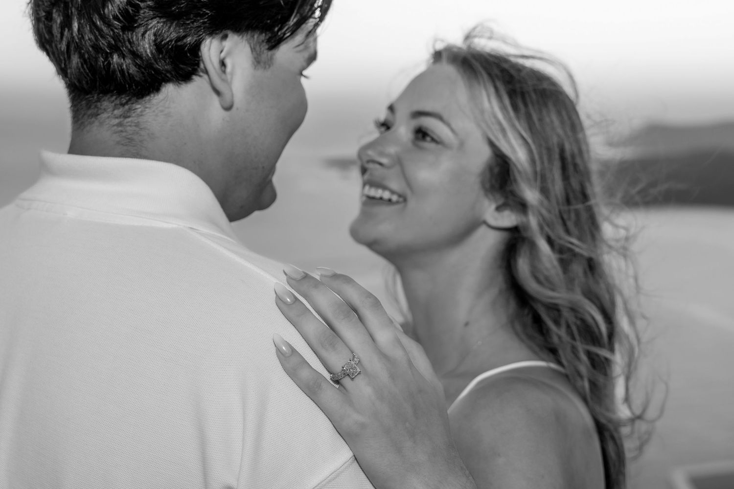 Groom standing with wedding ring on a terrace in Santorini, bride excited and surprised, smiling during the proposal