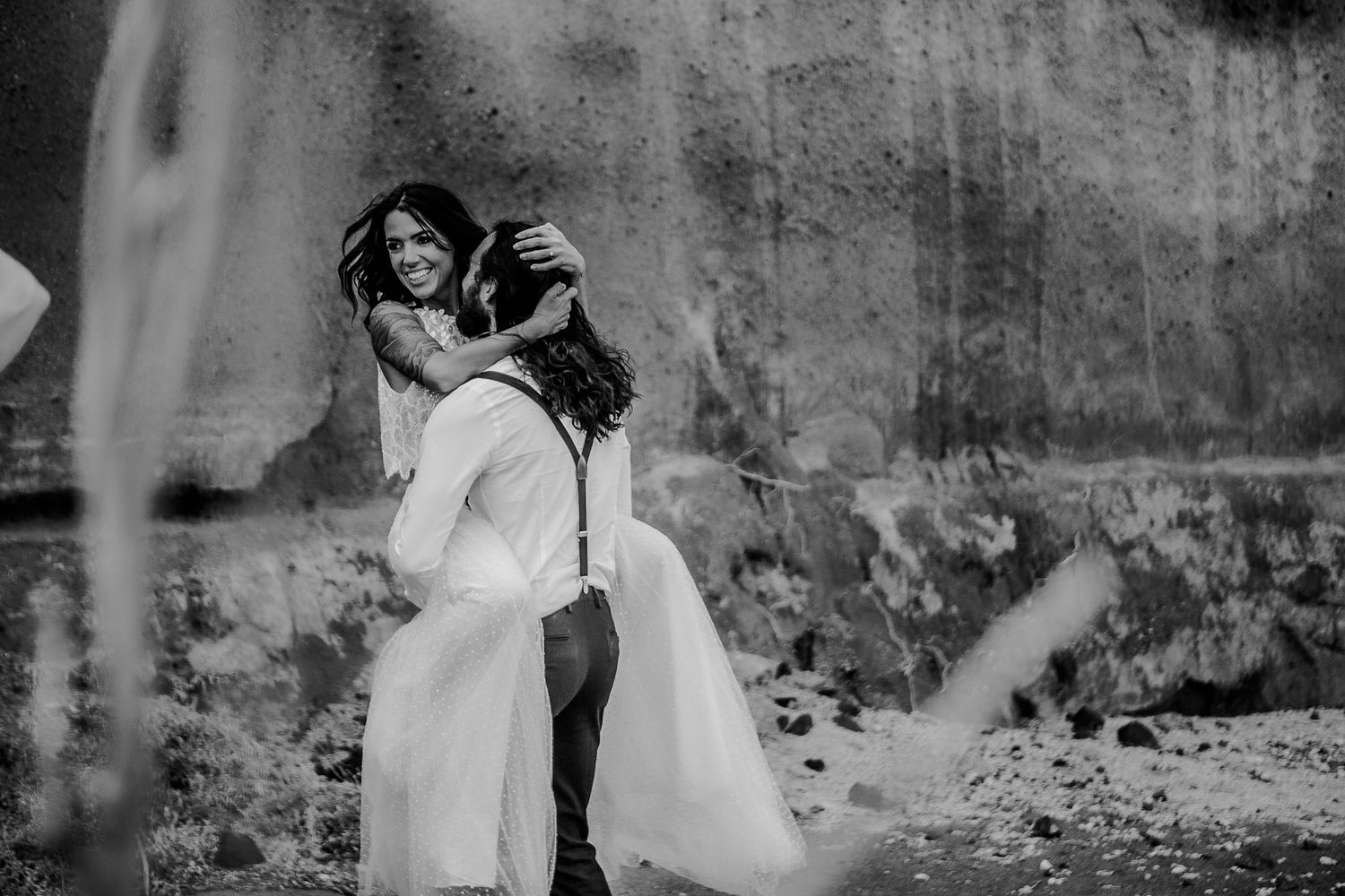 Elopement moment captured at Santorini's wild lava rock formations, intimacy, love, and laughter in the air. The bride in a wedding dress.