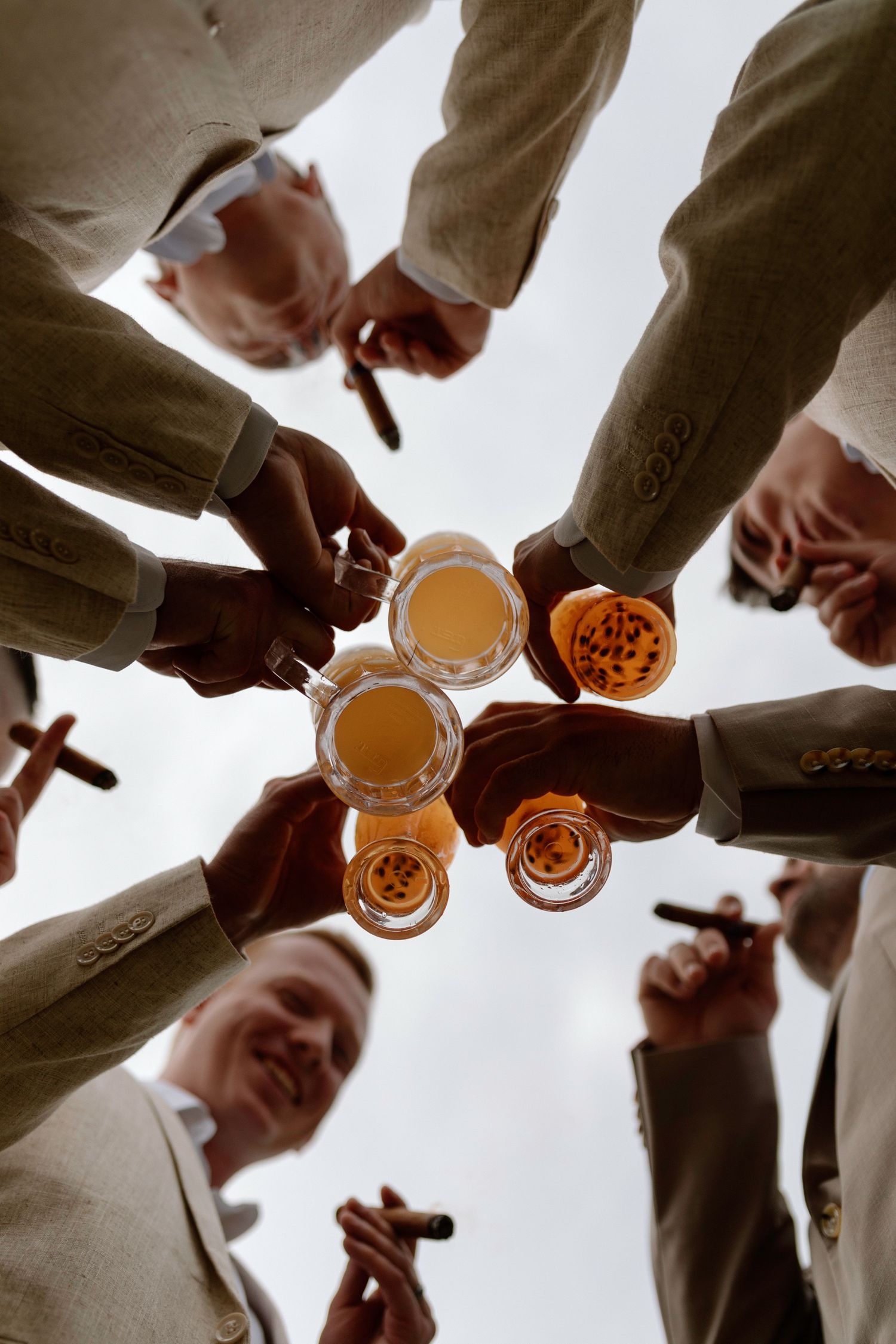 Low angle view of groomsmen toasting with whiskey glasses and cigars at wedding.
