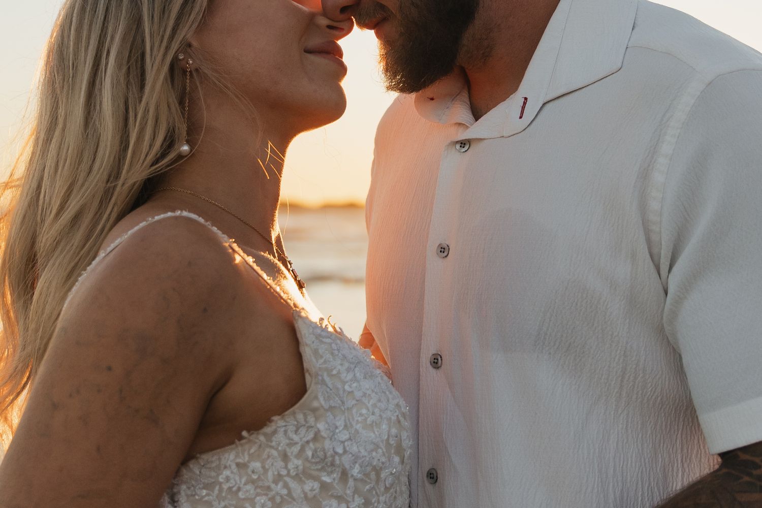 Close-up of a couple in wedding attire leaning in for a kiss during a warm beach sunset.
