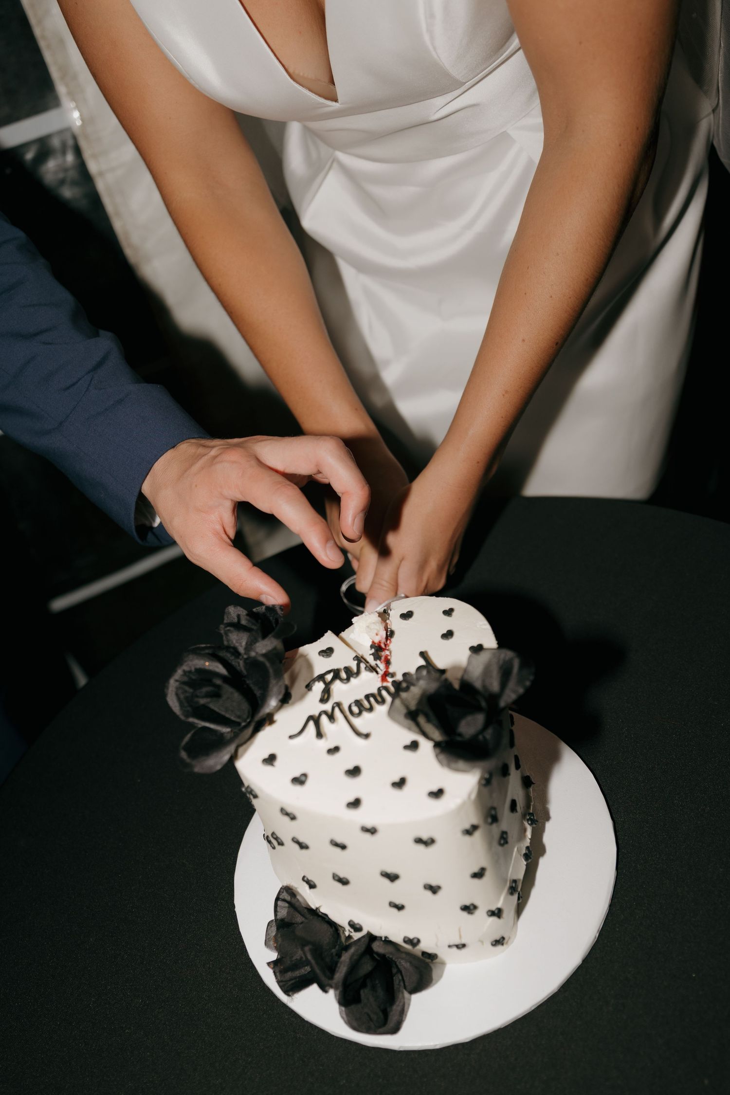 Bride and groom cutting white heart-shaped wedding cake decorated with black bows.