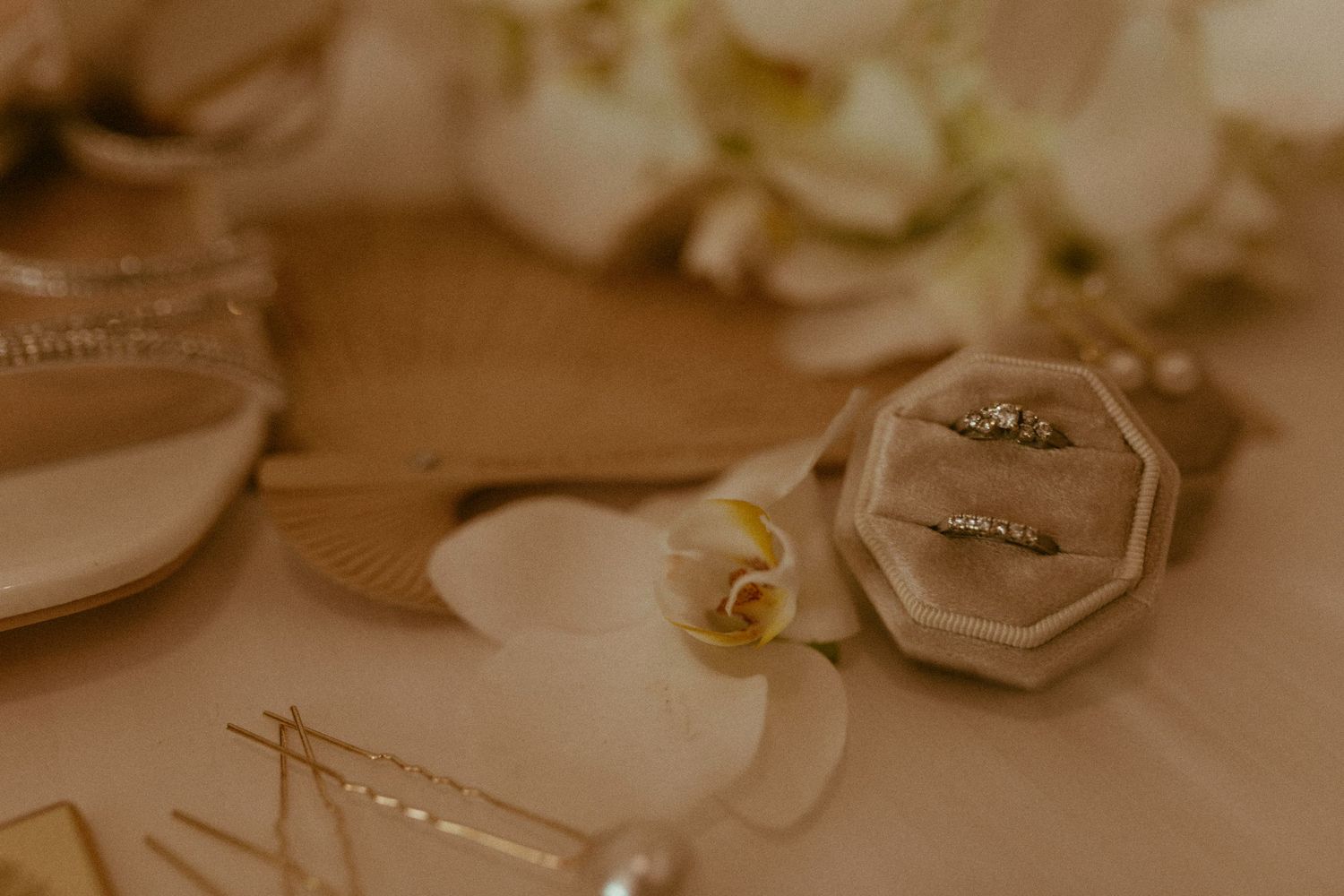 Gold wedding rings displayed in velvet box with white orchid flowers and jewelry on table.