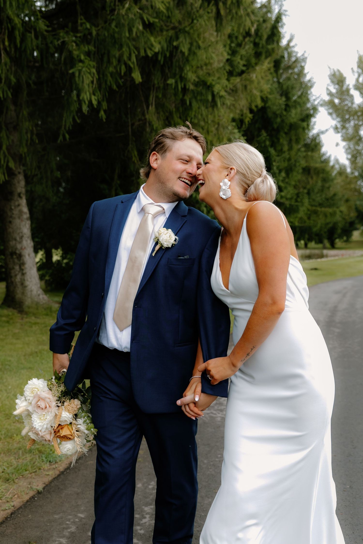 Bride and groom sharing romantic moment walking hand in hand on tree-lined path at outdoor wedding.