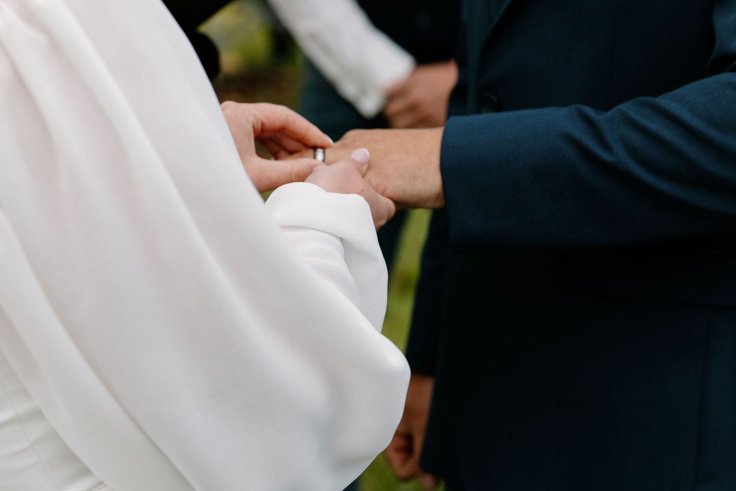 Close-up of groom placing wedding ring on bride's finger during outdoor ceremony.