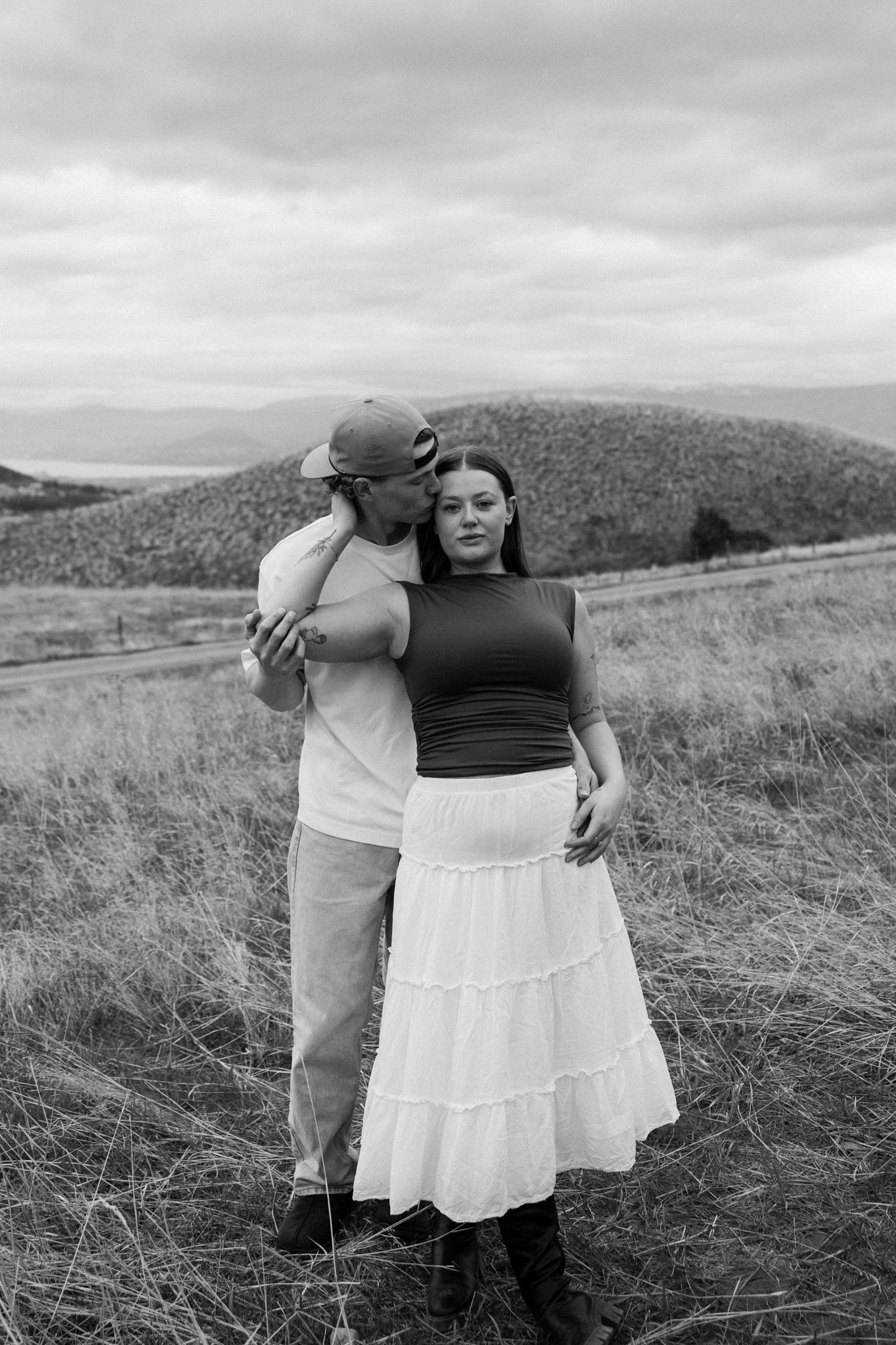Black and white photo of a couple embracing in a mountain meadow.