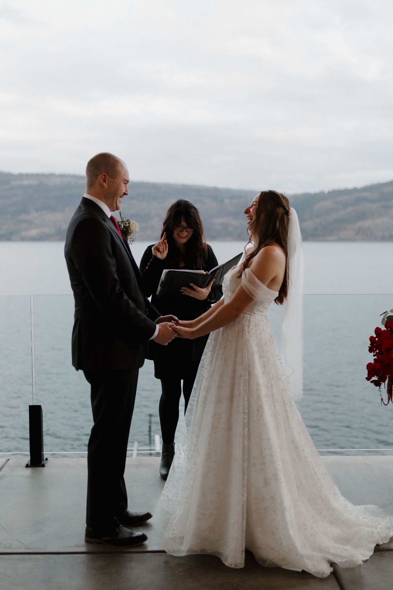 Bride and groom exchanging vows with officiant overlooking a stunning lake during outdoor ceremony.