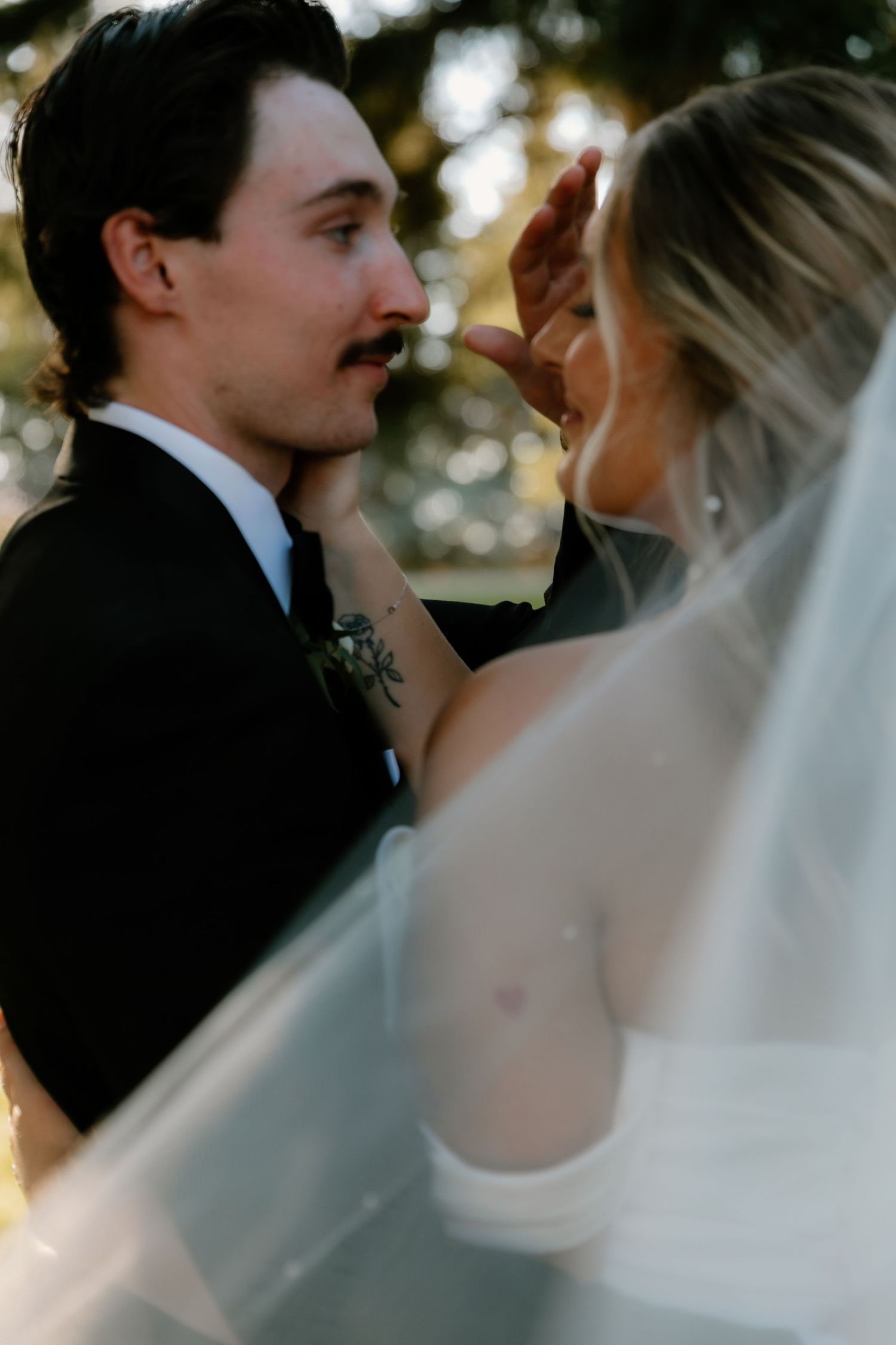 Romantic wedding portrait of bride and groom under flowing veil in warm golden outdoor light.