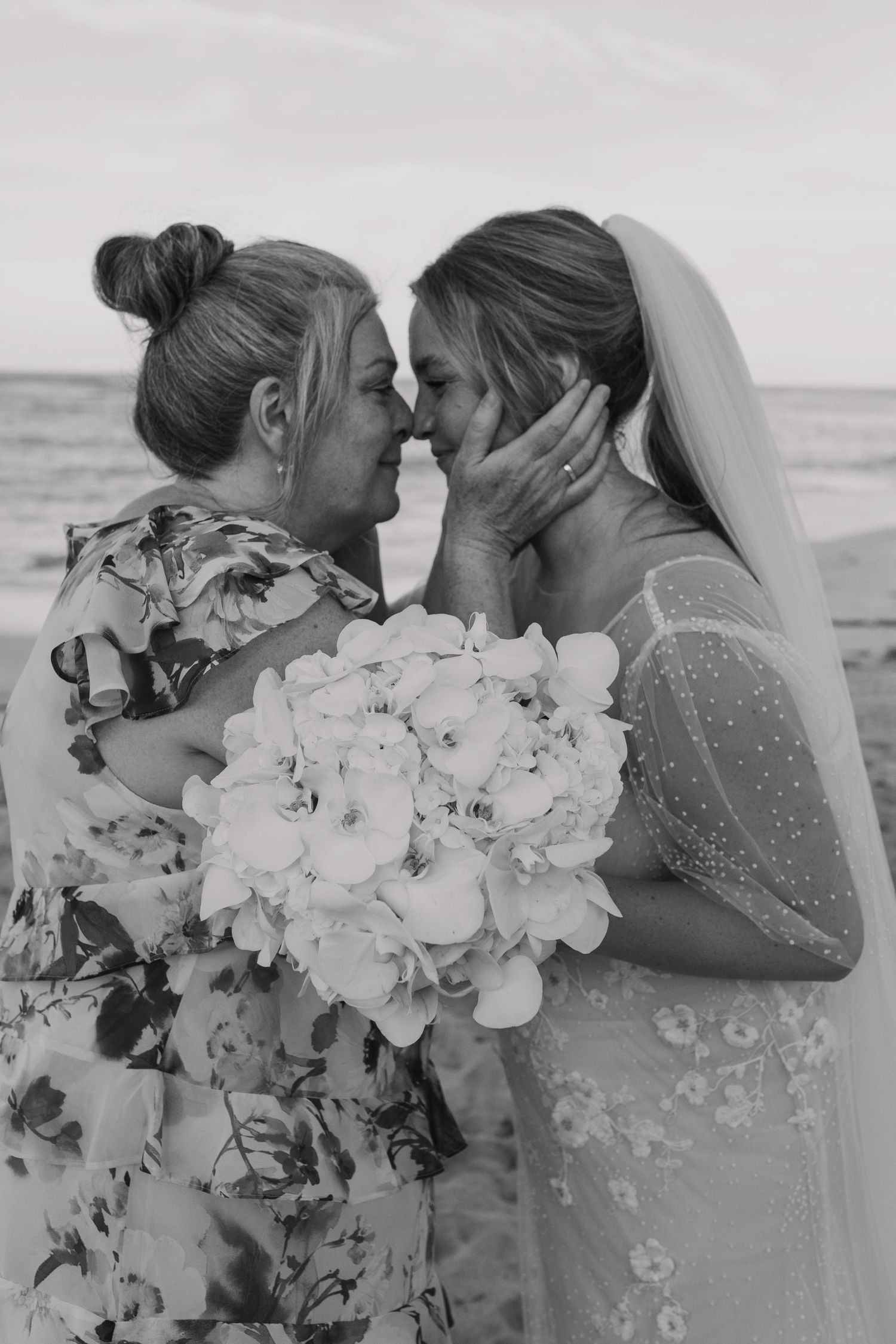 Black and white photo of bride and mother sharing tender moment with bouquet.