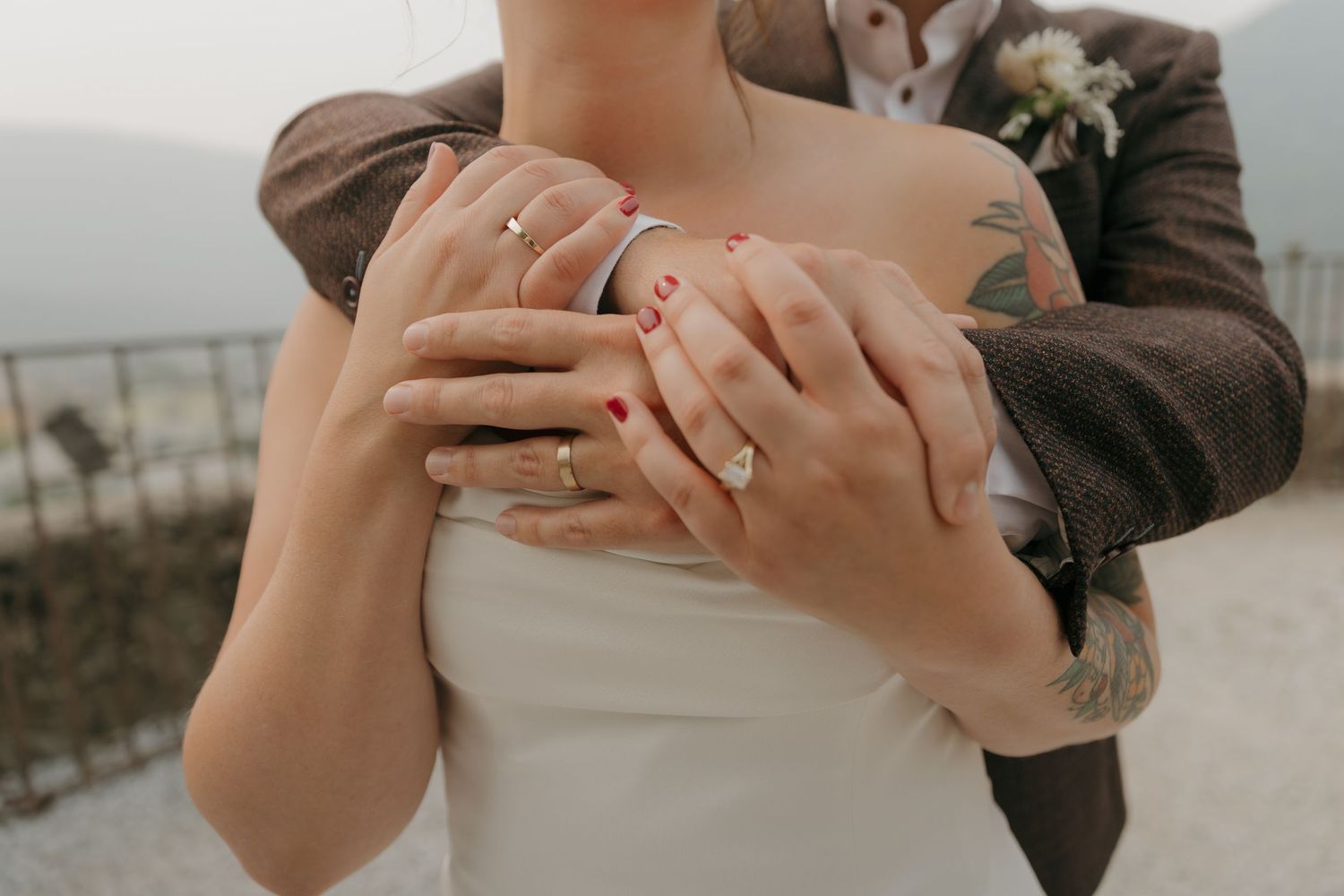Close-up of bride and groom displaying wedding rings, bride with red nails and sleeve tattoo.