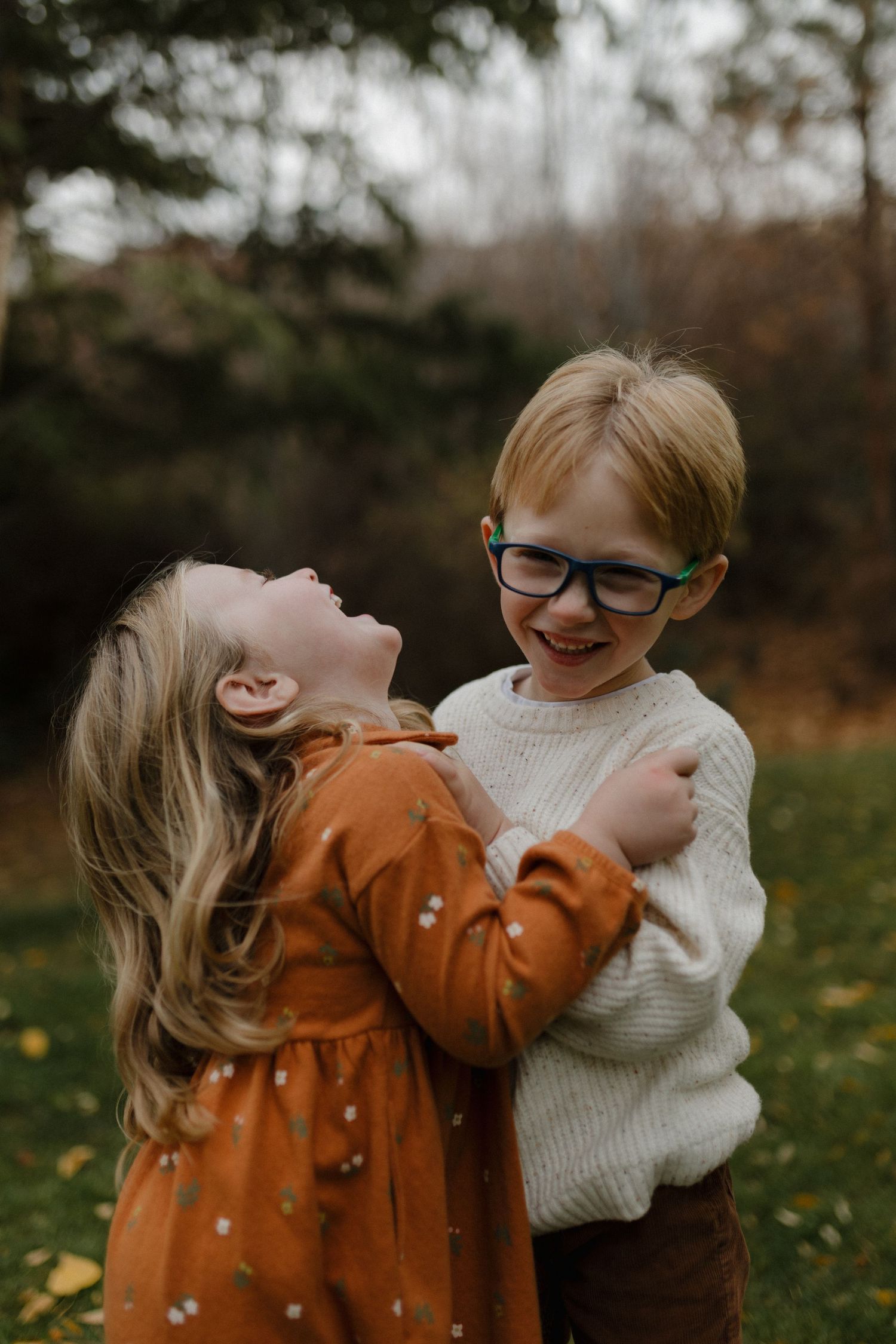 Two young children laughing and hugging each other playfully in an autumn outdoor setting.