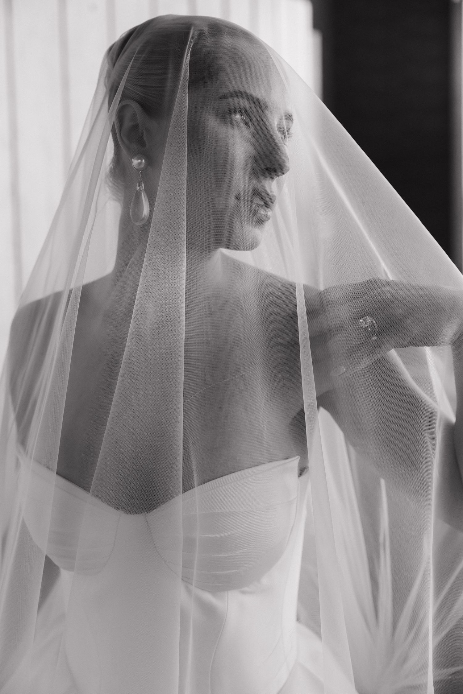 Elegant bride draped in a sheer wedding veil, captured in a timeless black and white portrait.