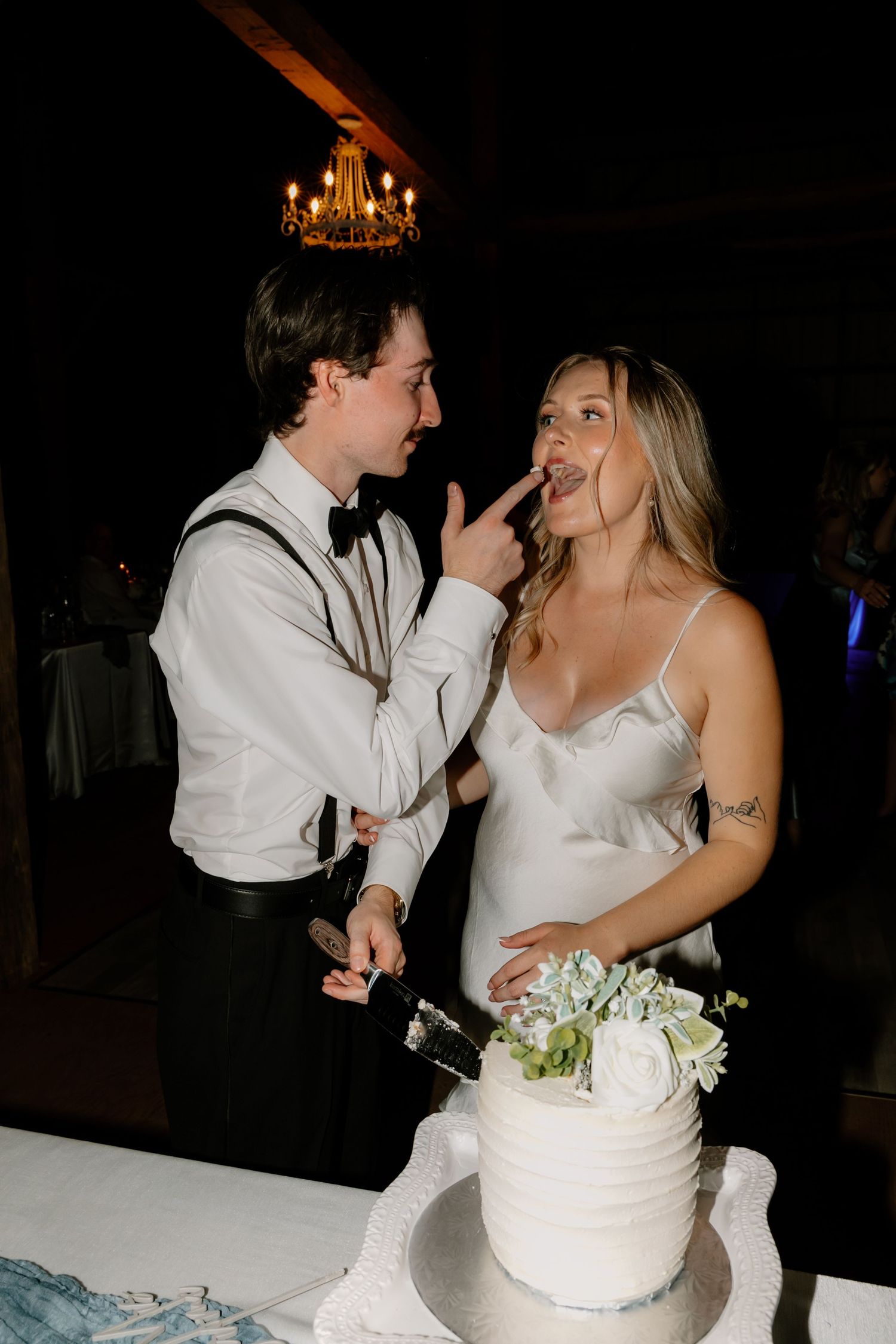 Bride and groom share playful cake cutting moment, groom feeding bride at elegant wedding reception.