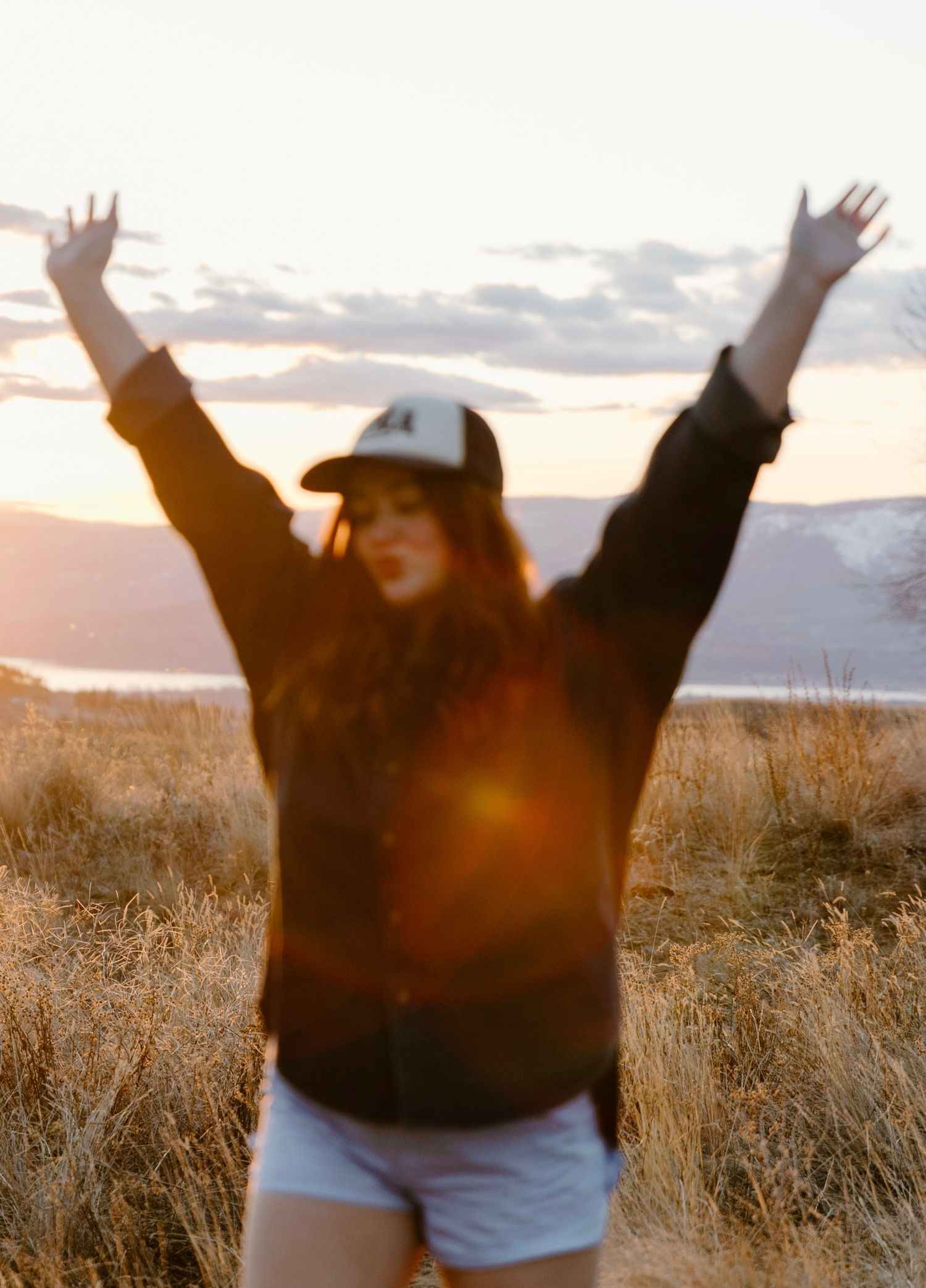 Woman raising arms joyfully at sunset in a golden field with lens flare.