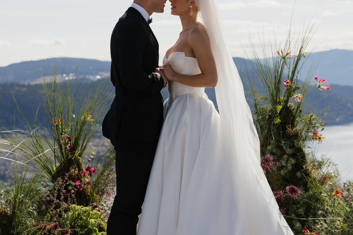 Bride and groom share a romantic moment outdoors with scenic lake and mountain views at their wedding ceremony.