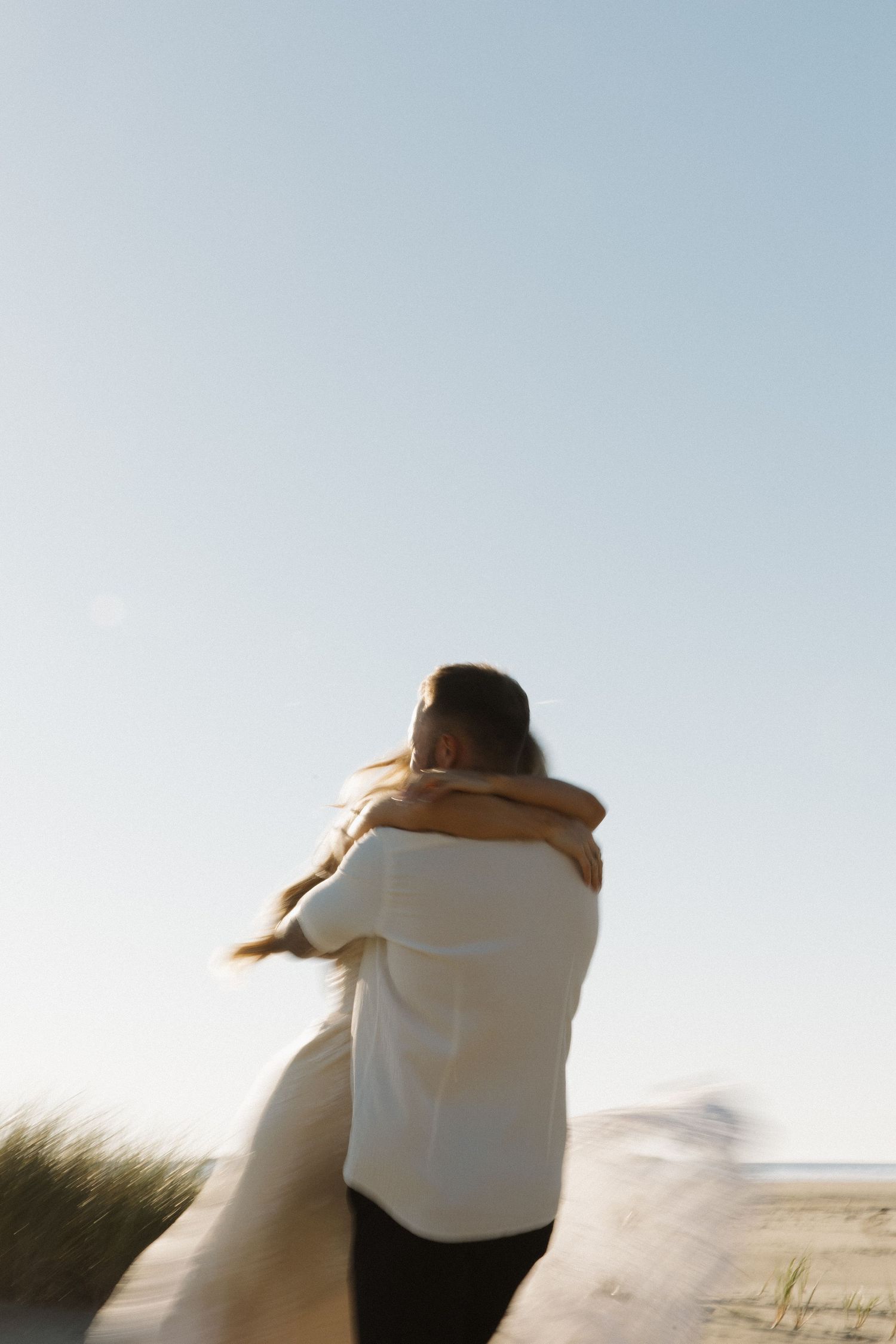 Couple embracing and spinning on a beach under a clear blue sky.