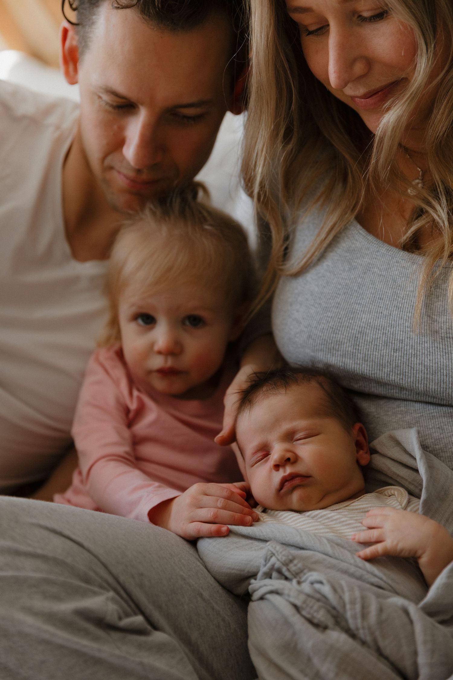 Parents lovingly gazing at newborn baby while toddler rests beside them on a cozy bed.