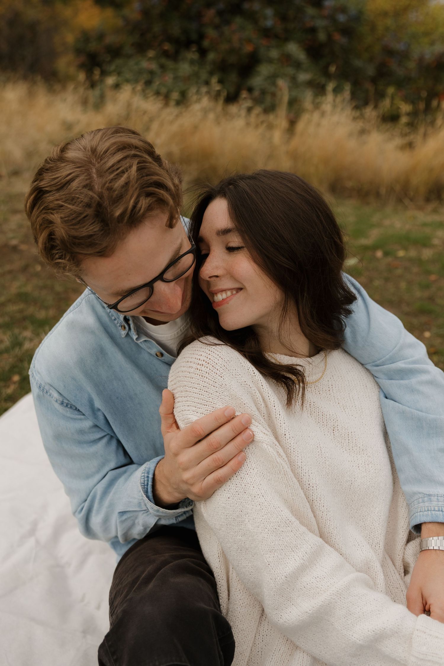 Couple sharing a tender moment outdoors in autumn, man embracing smiling woman in cream knit sweater.