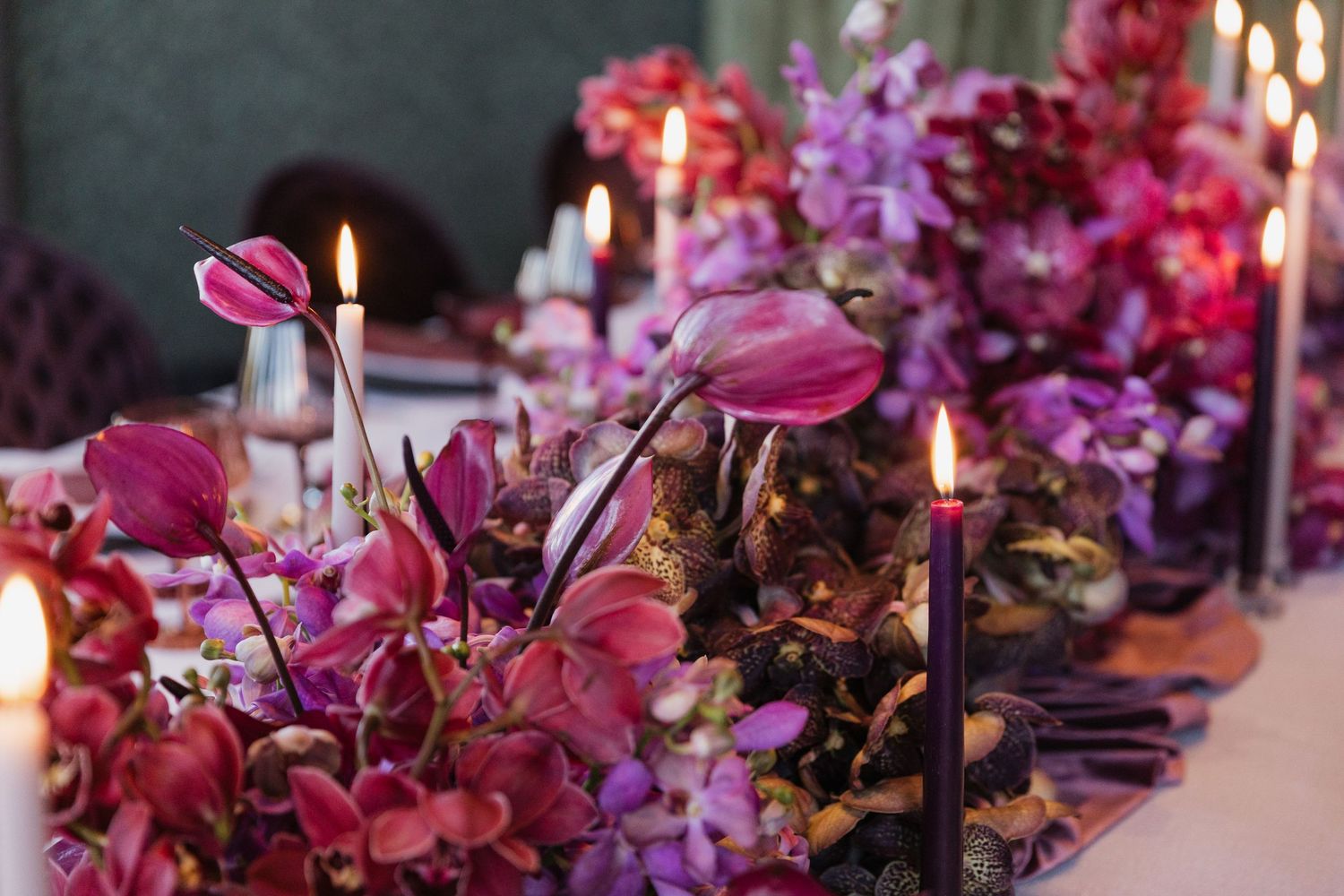 Close-up of lush wedding tablescape featuring pink anthurium, orchids, and lit dark candles.
