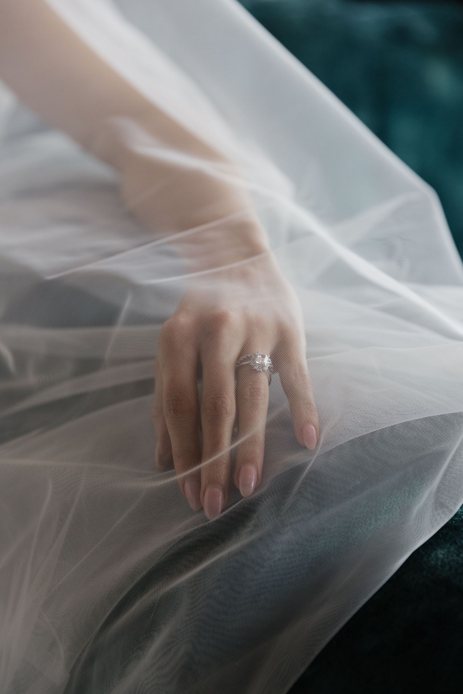 Close-up of bride's hand wearing a sparkling diamond engagement ring draped over soft white tulle fabric.