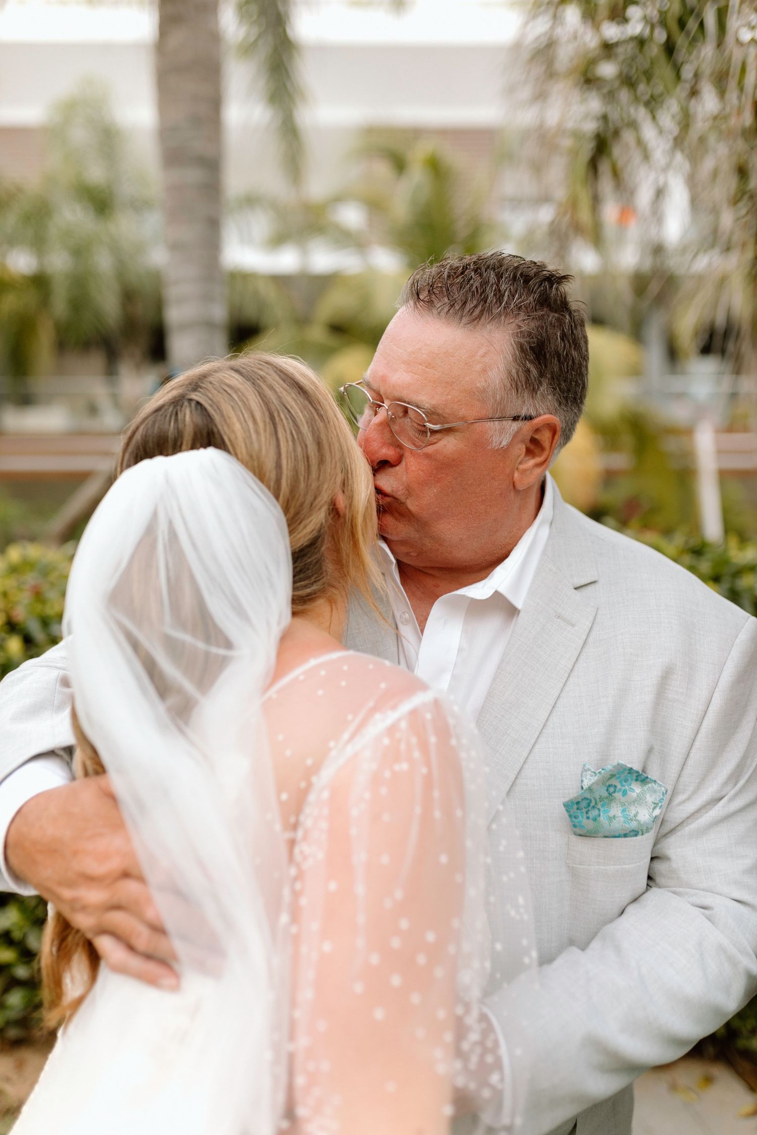 Emotional father kissing bride on cheek during first look moment at tropical destination wedding.