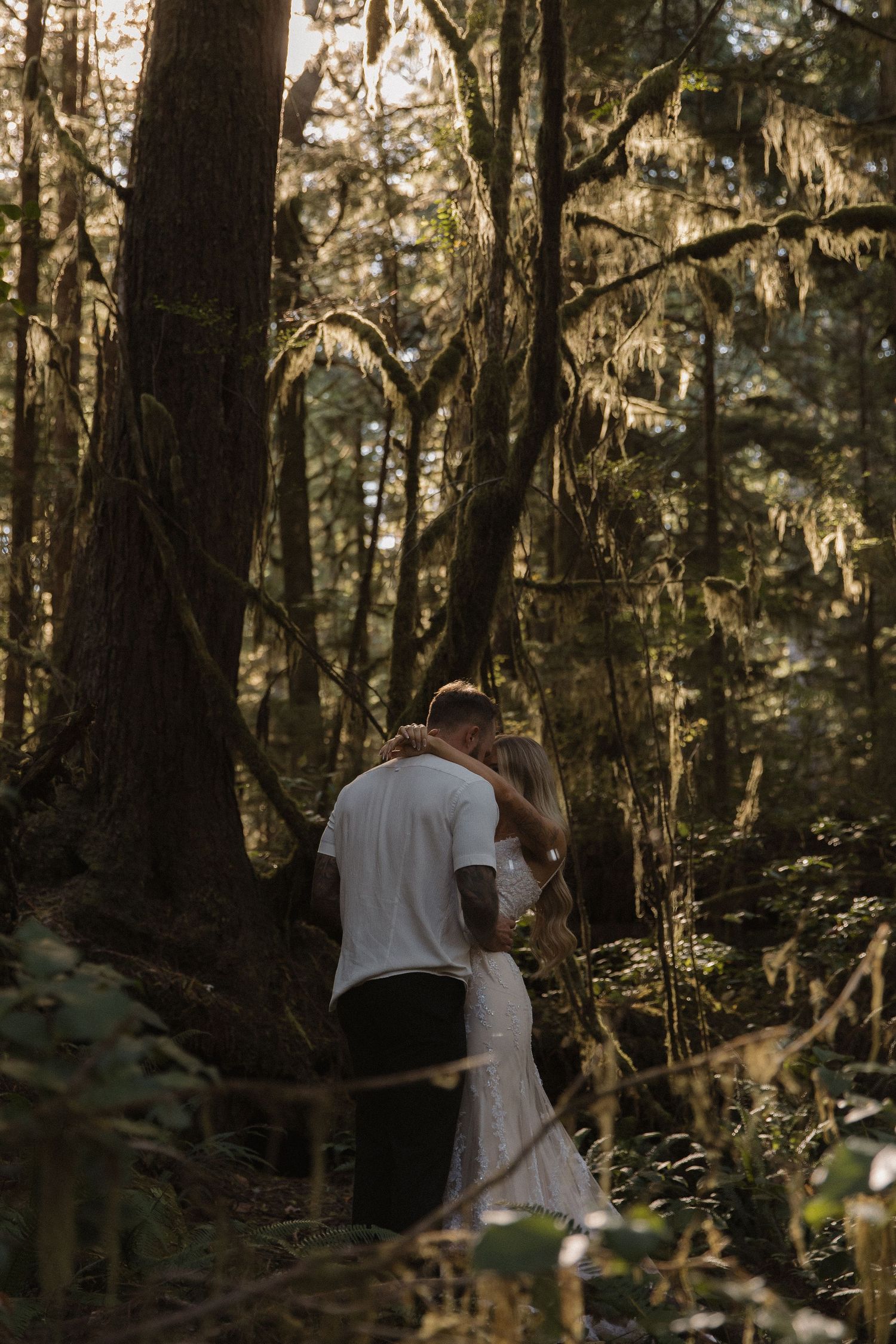 Bride and groom sharing a kiss surrounded by lush mossy forest trees.