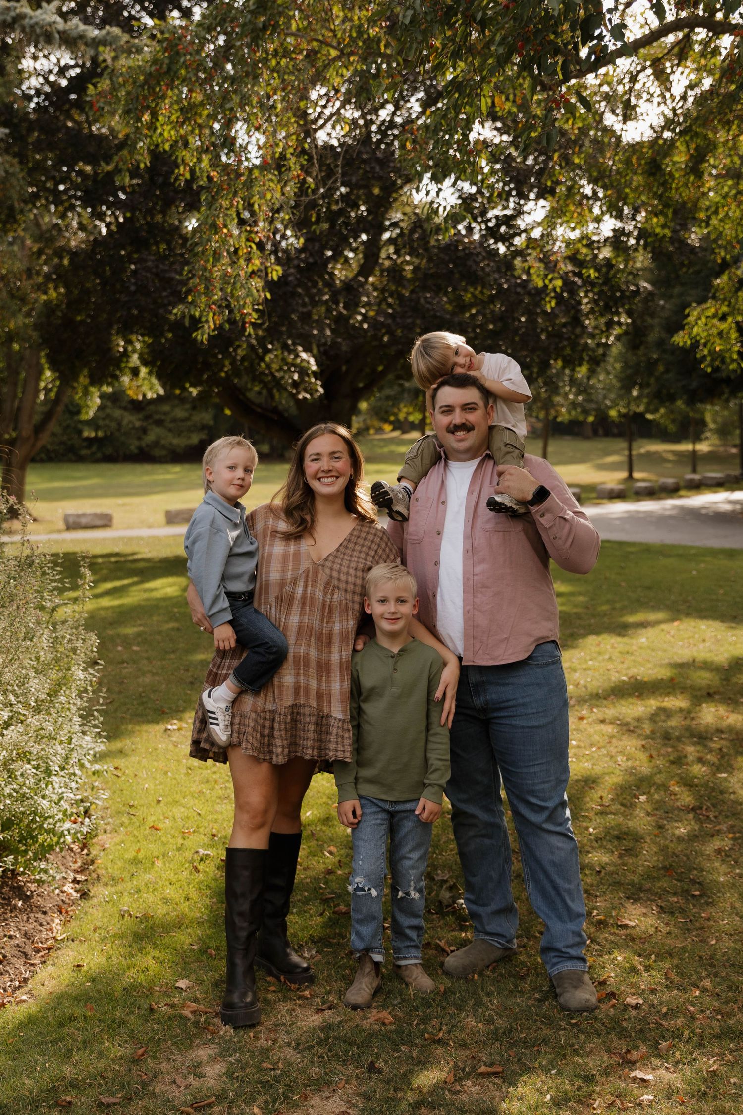 Happy family of five posing outdoors in a lush green park during autumn.