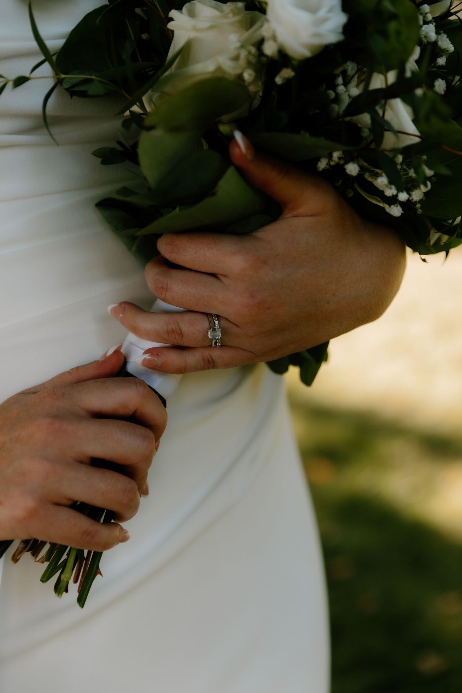 Close-up of bride's hands holding white and green wedding bouquet, diamond ring visible on finger.