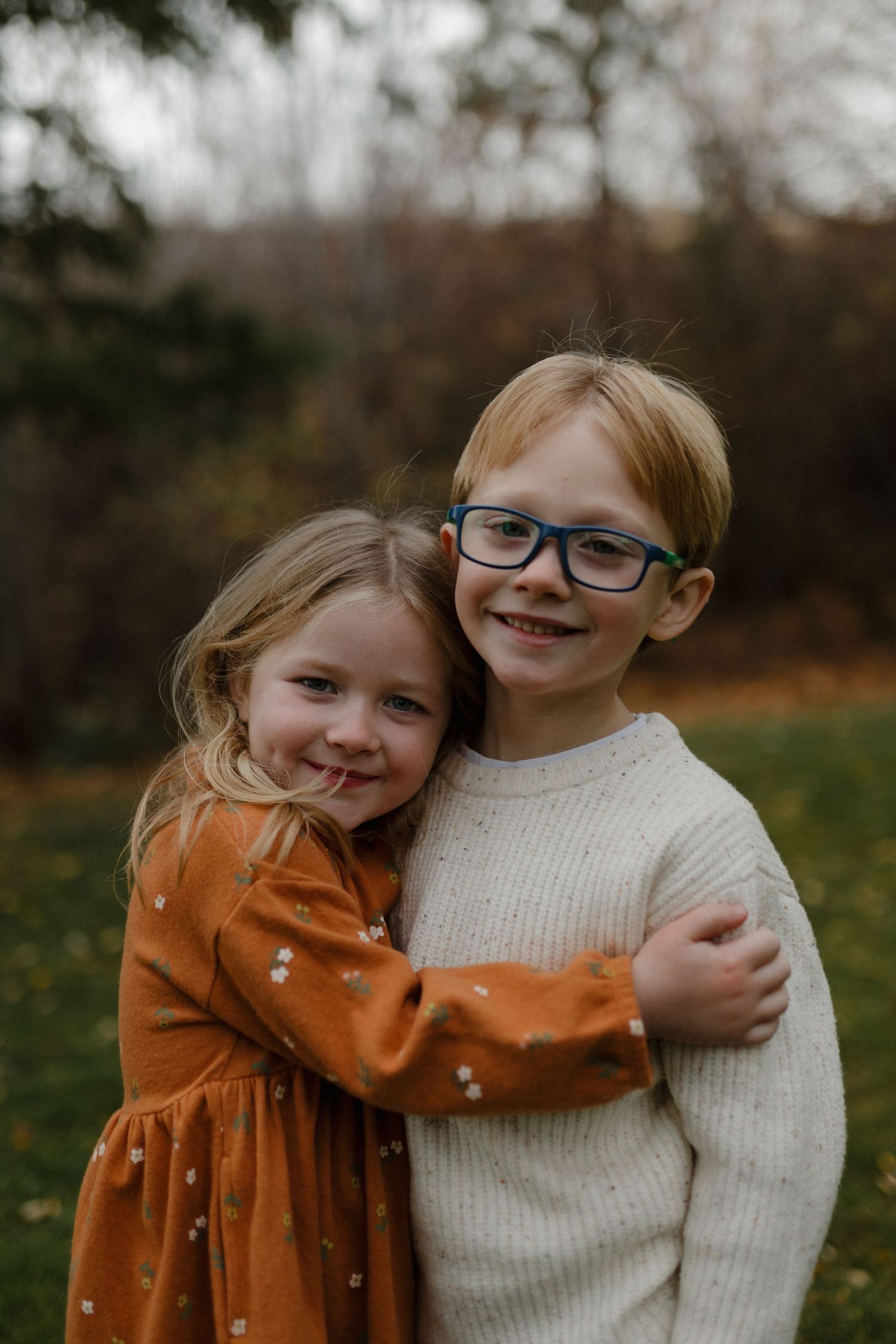 Two young siblings hugging and smiling outdoors in an autumn garden setting.