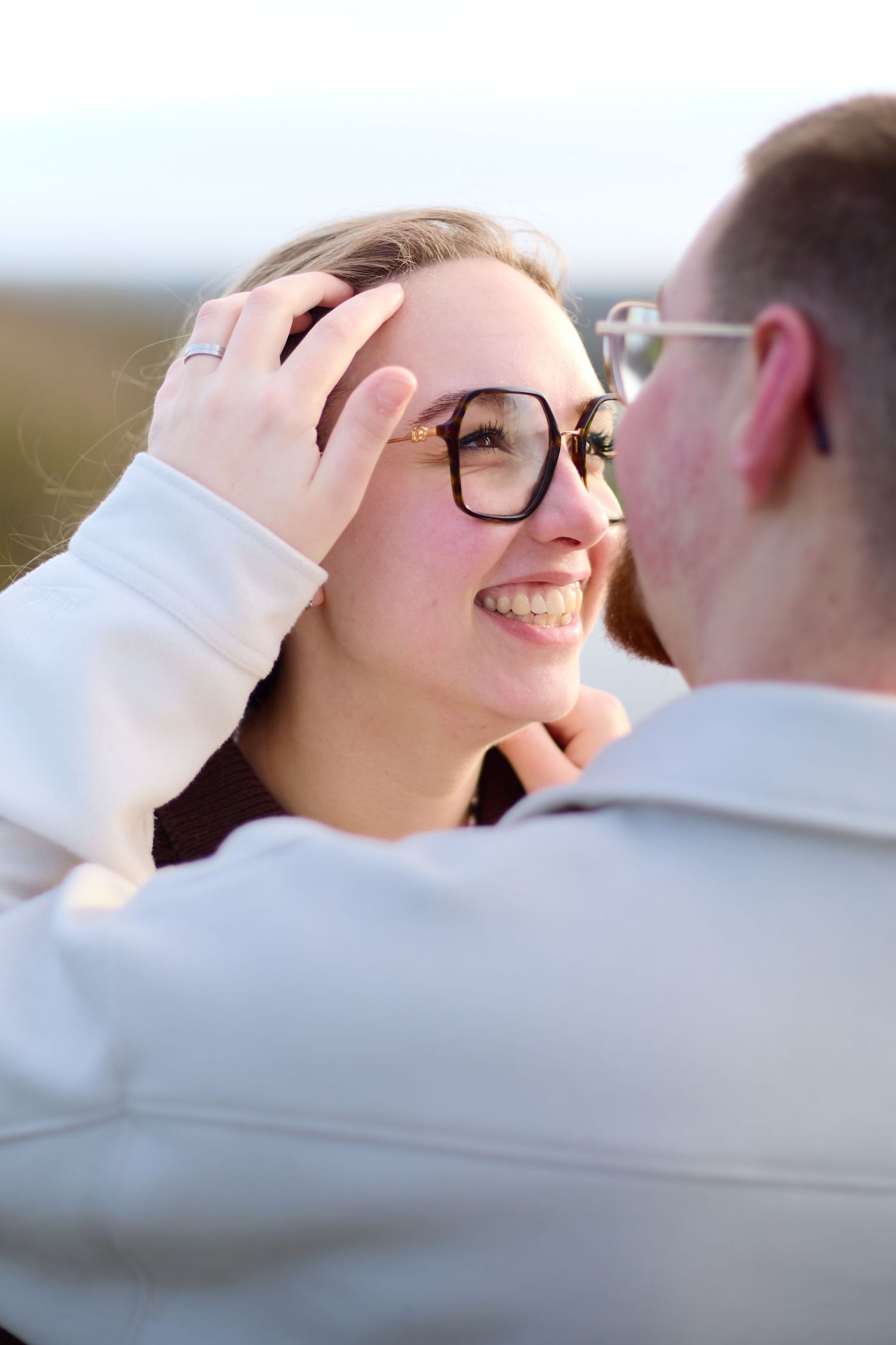 Tender moment captured between couple with glasses against natural outdoor backdrop.