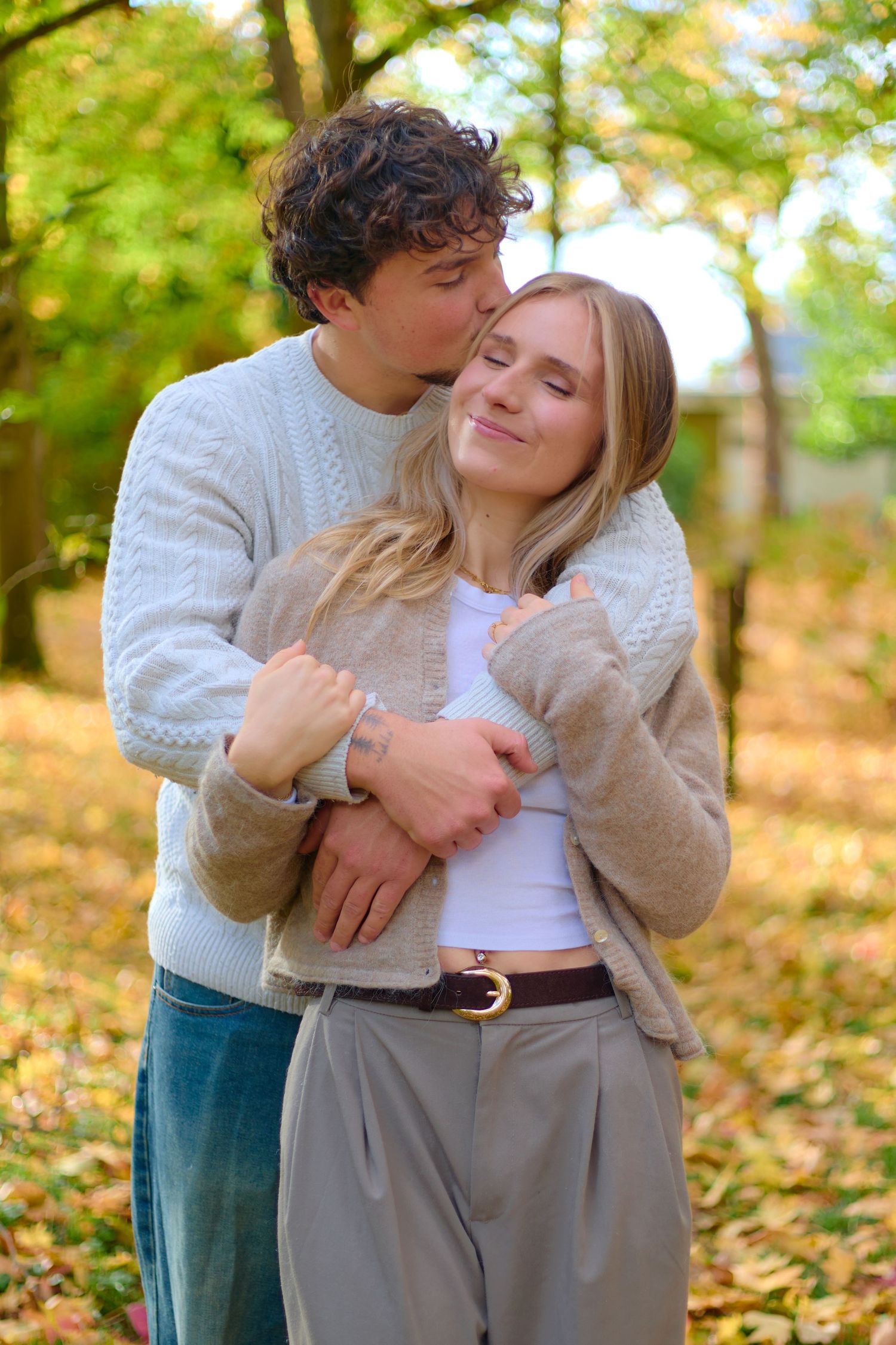A sweet autumn embrace between two people in cozy sweaters among fallen leaves.