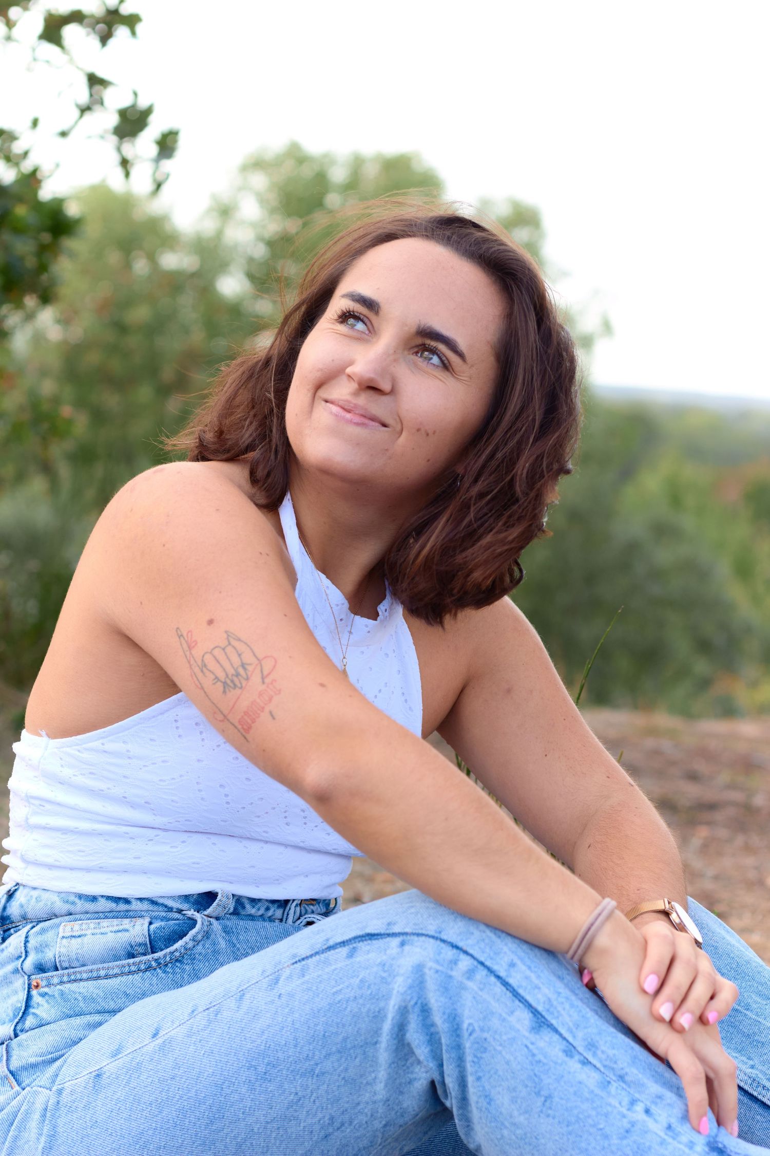 A woman in a blue tank top and jeans poses casually outdoors during a photo session.
