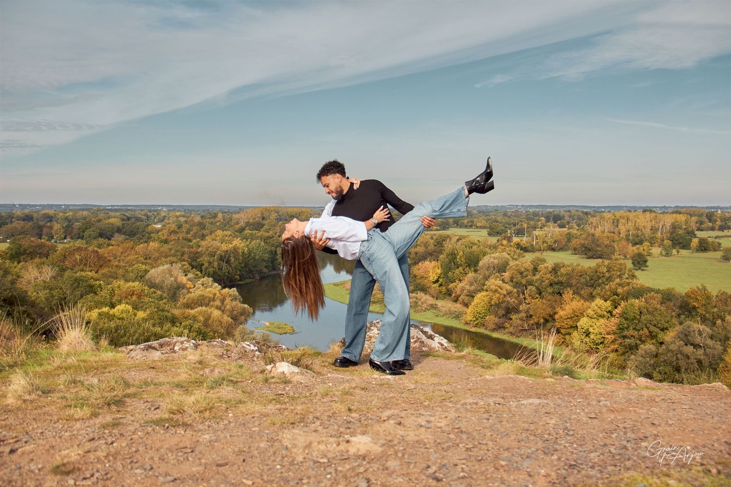 A playful dip pose captured on a hilltop overlooking an autumn landscape.