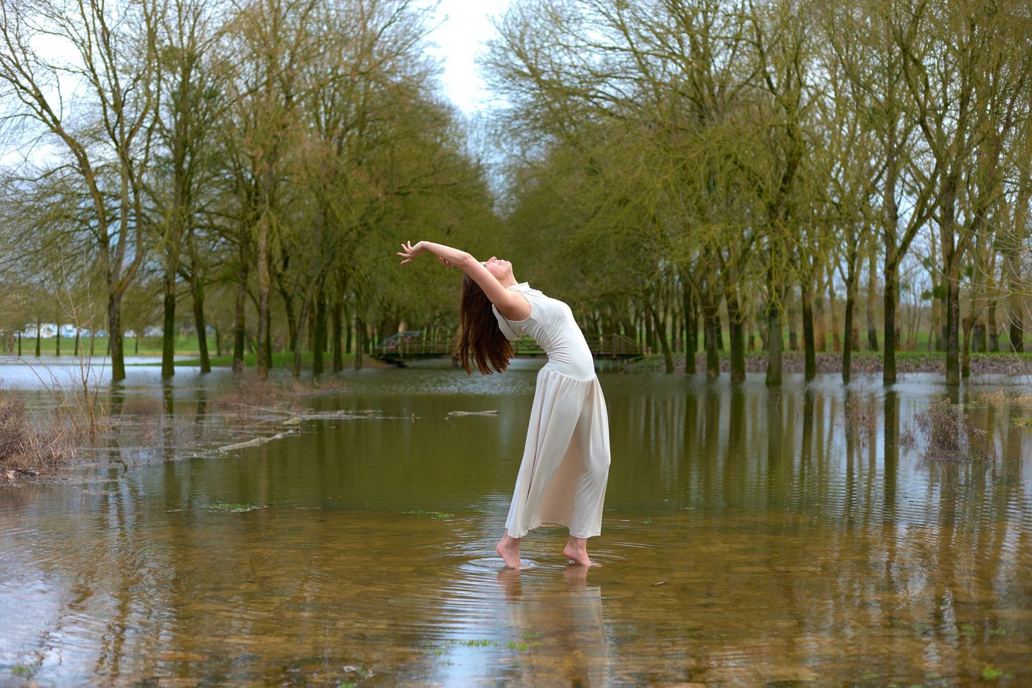 Person in white dress creating ethereal poses among flooded trees in a dreamy landscape.