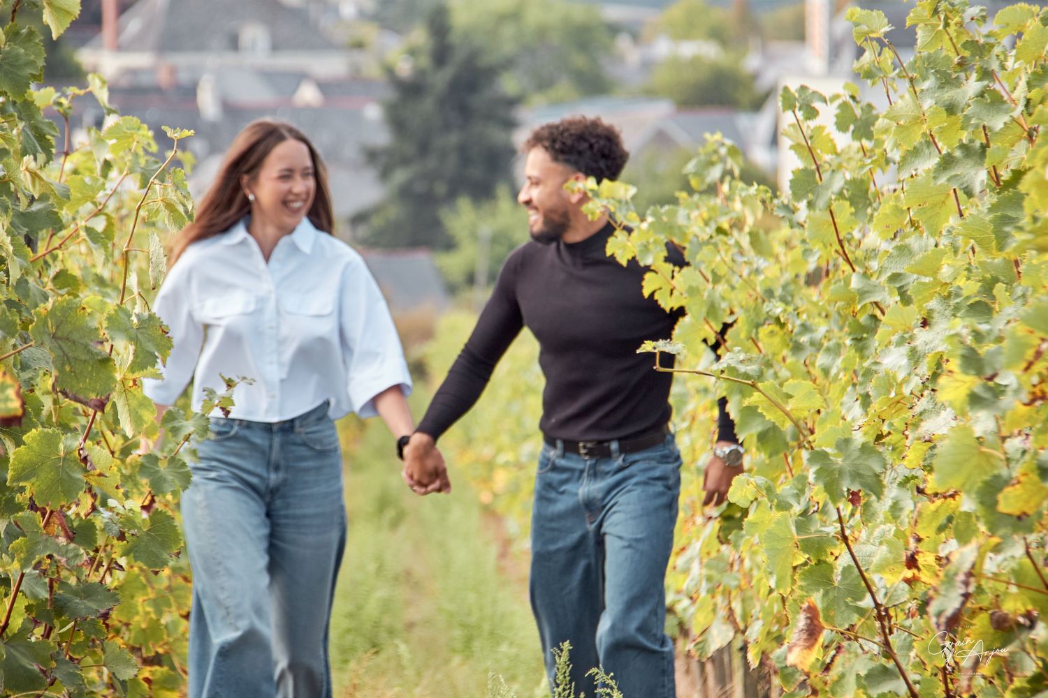 A joyful couple holding hands while walking through vineyard rows on a sunny day.