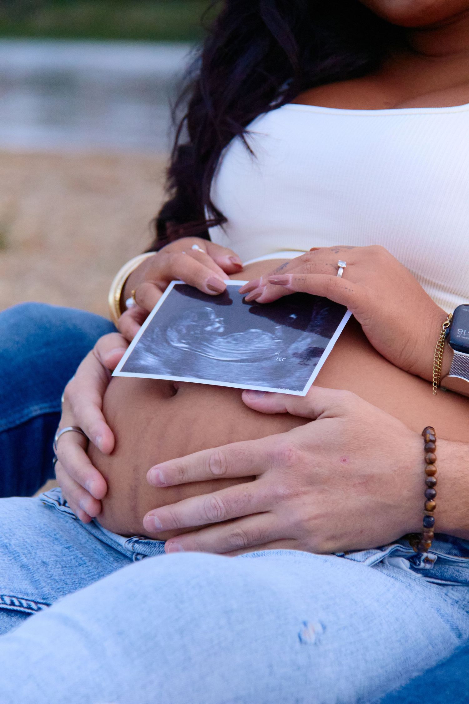Hands holding ultrasound photos against denim background.