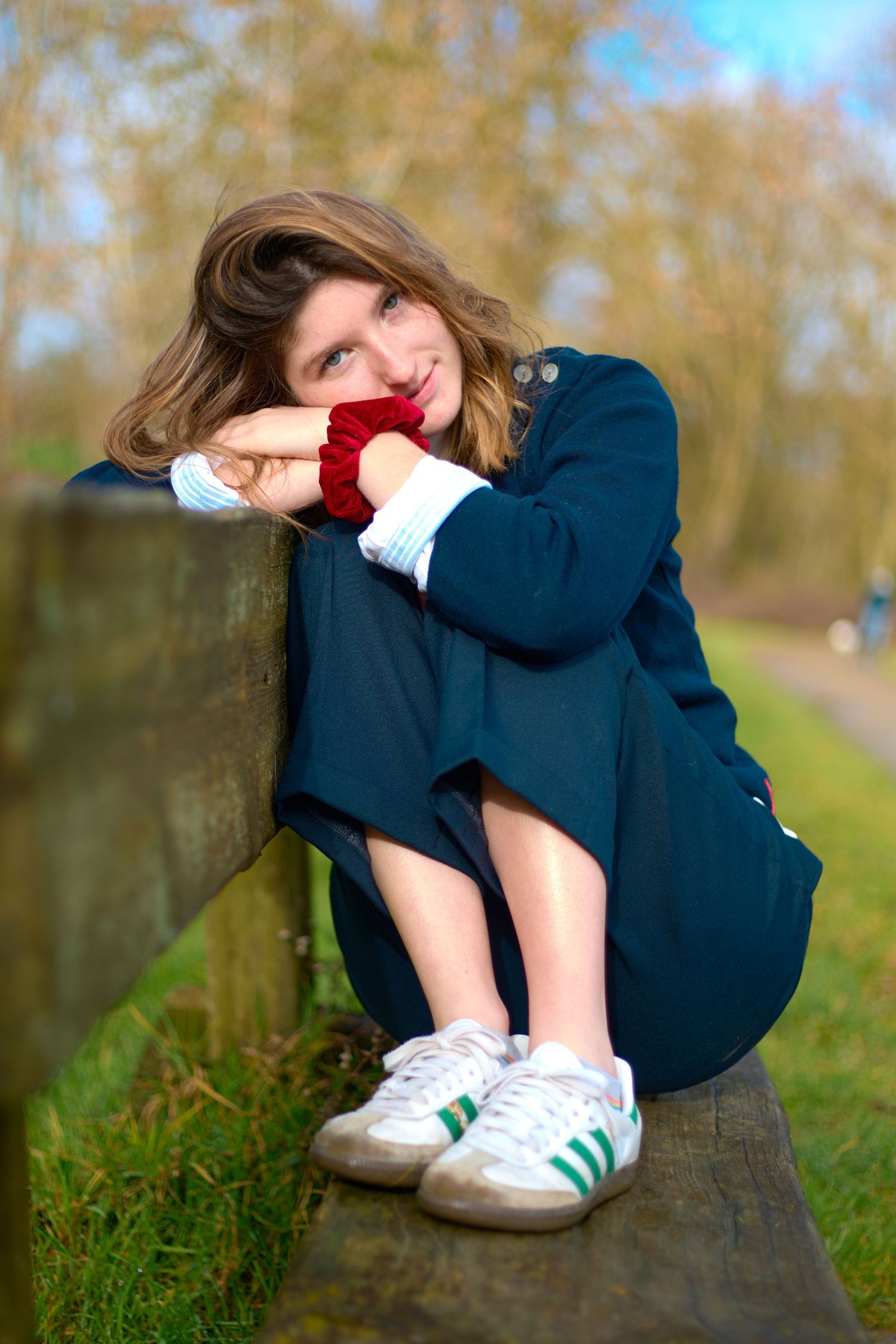 Playful portrait on wooden bench wearing navy outfit and white sneakers in park setting.