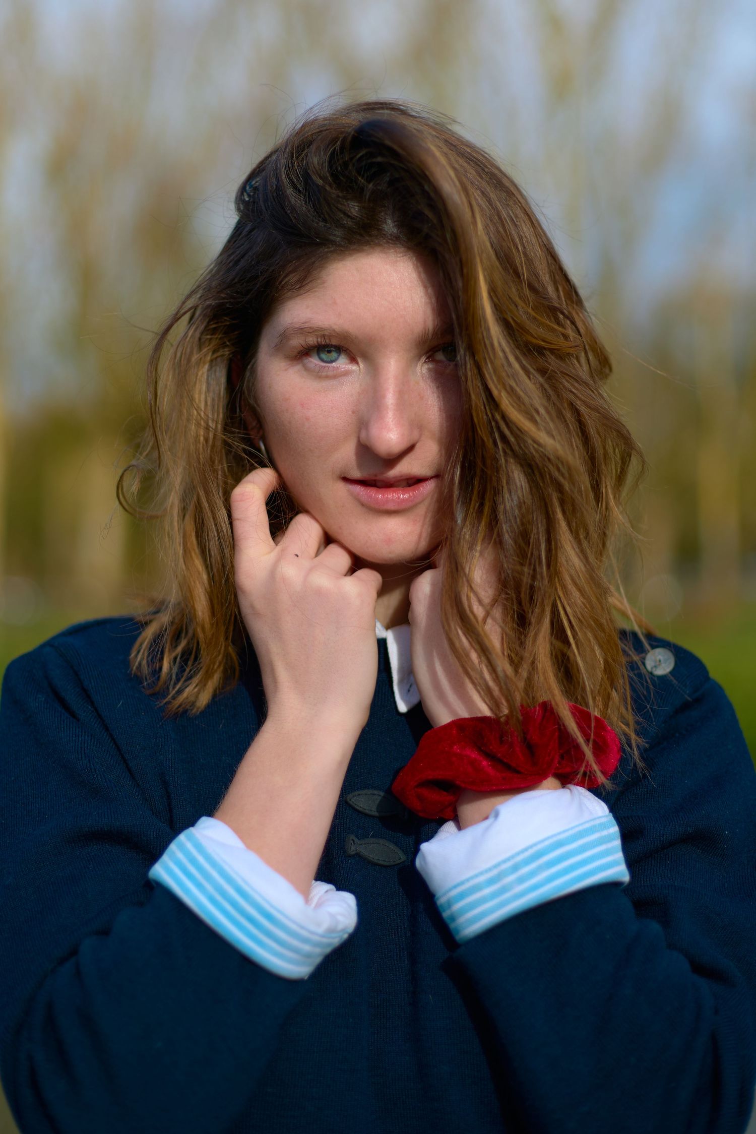 Portrait of person in navy jacket with windswept hair against natural background.