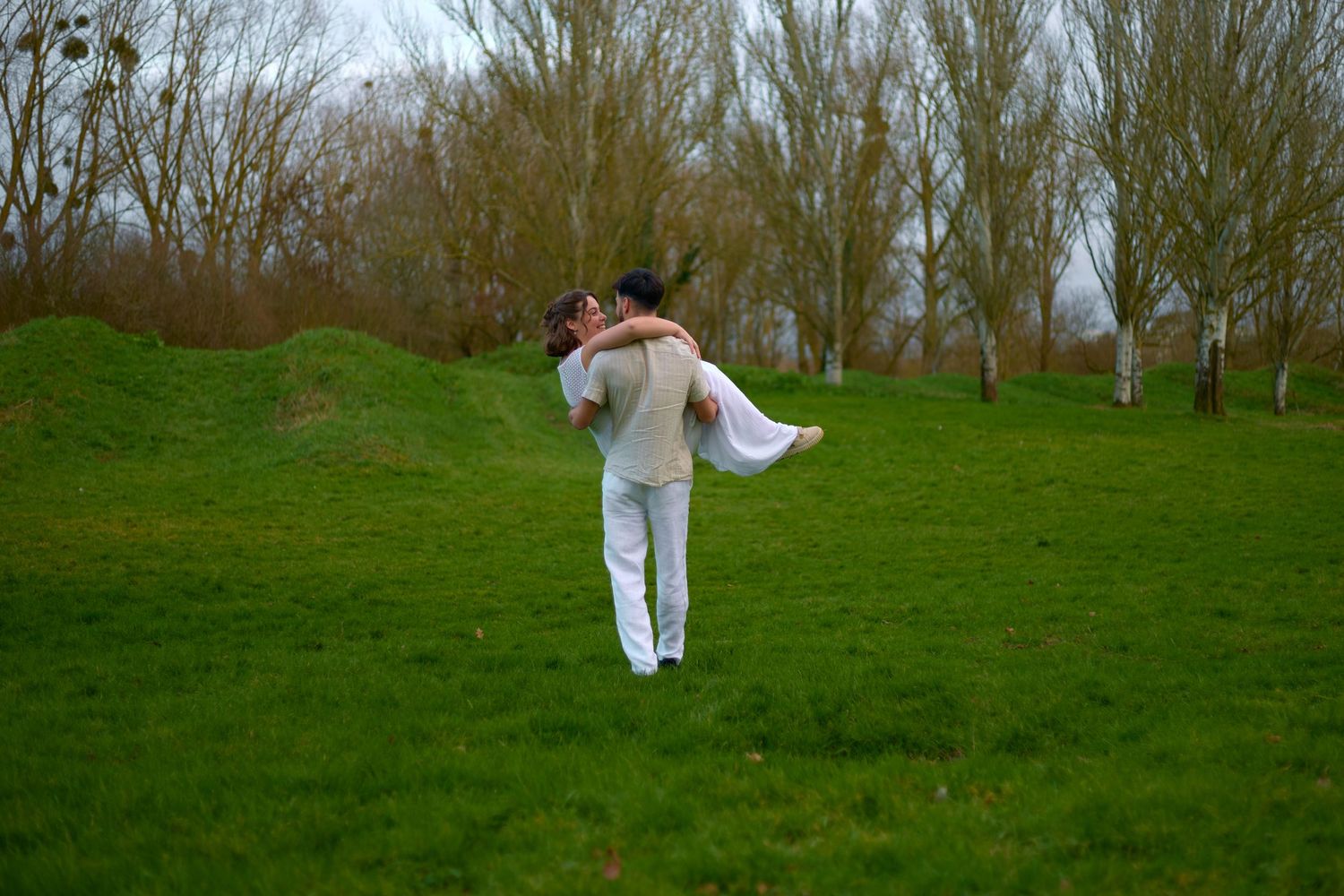 Person in white clothing practices martial arts moves on a lush green hillside in springtime.