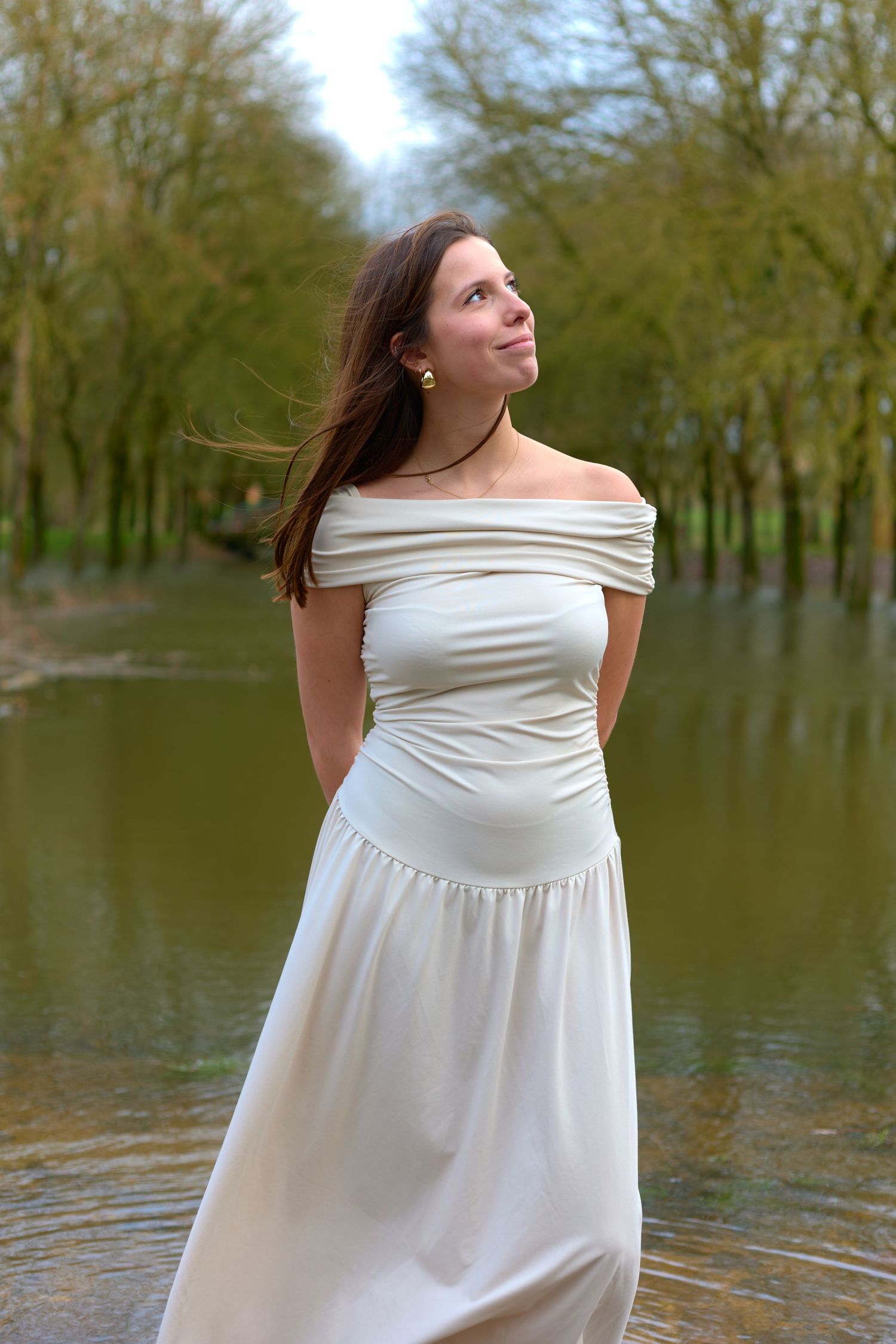 Elegant portrait in white off-shoulder dress by flooded woodland area.
