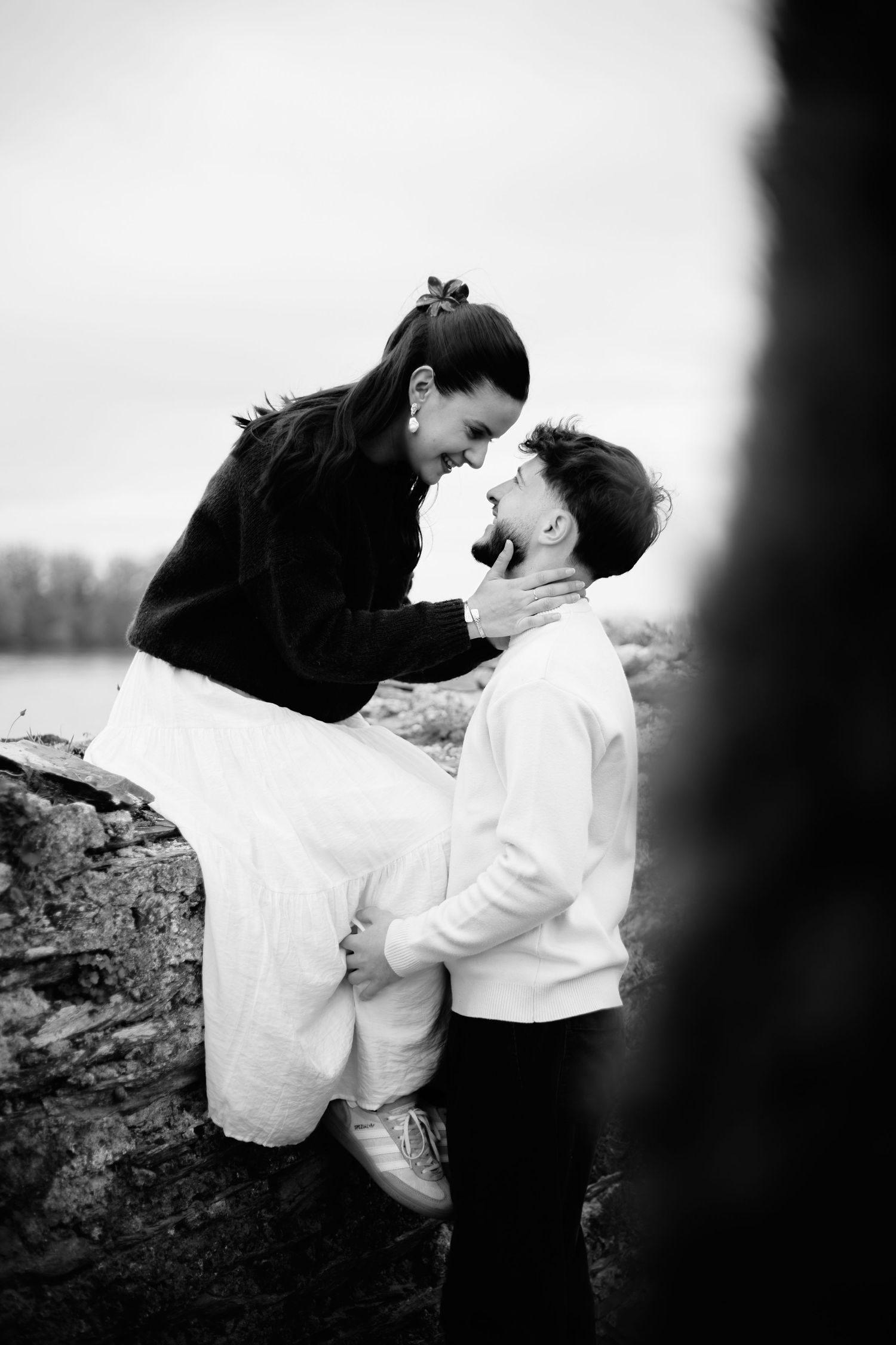 Black and white photo of a mother and son sharing a tender moment, laughing together outdoors near a stone wall.