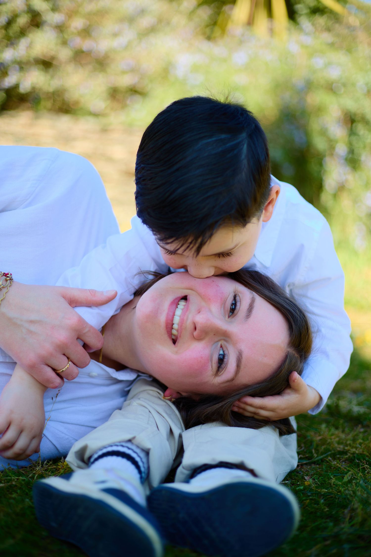 A young boy kisses his smiling mother while they play together on green grass outdoors.