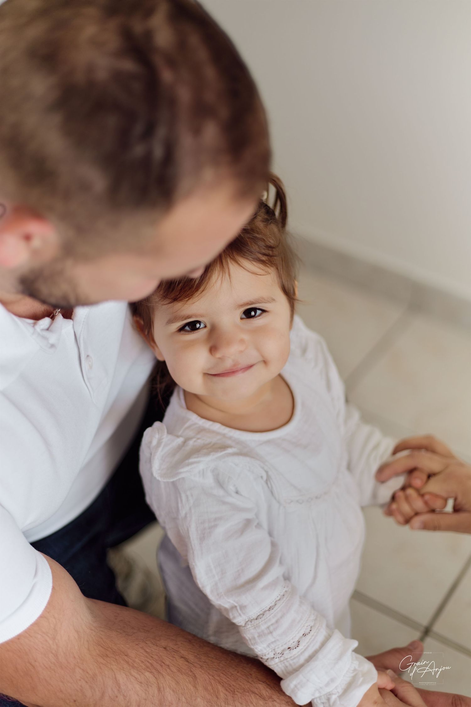 A sweet candid moment between parent and toddler in white clothing indoors.